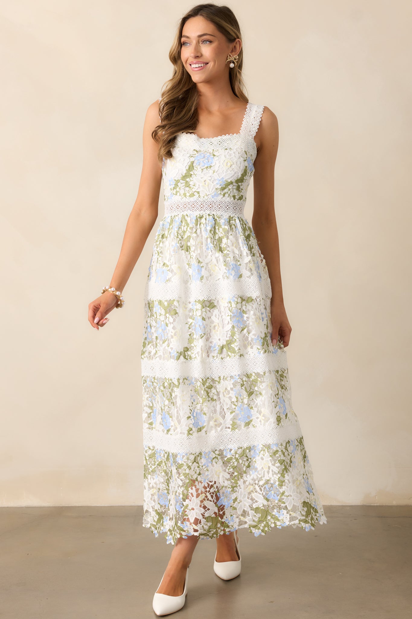 An ivory dress with a straight neckline, floral embroidered overlay, and tiered embroidery design flows gracefully, with adjustable embroidered shoulder straps adding a delicate touch.