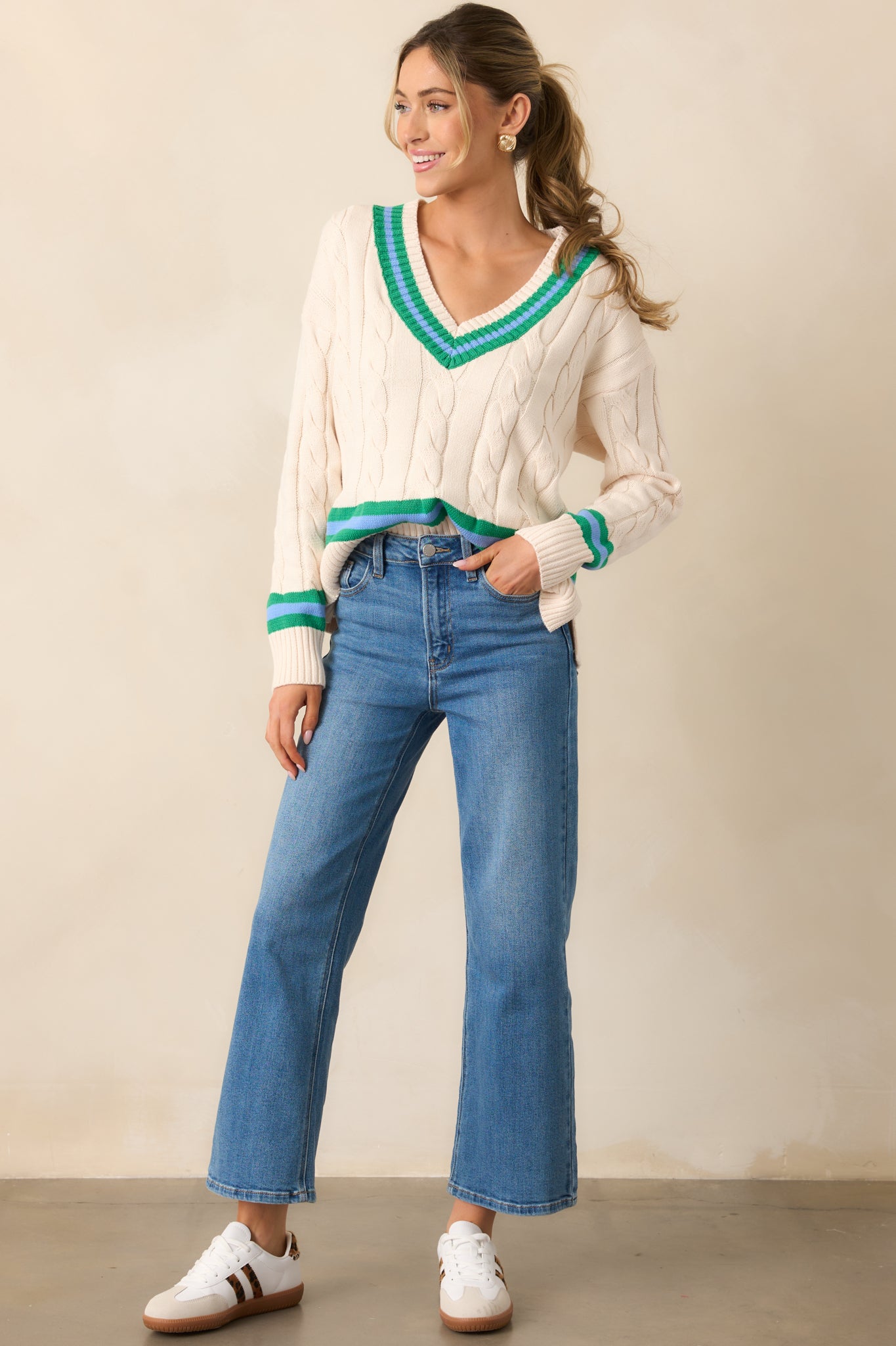 Front view of the ivory sweater showcasing its v-neckline, long sleeves, and cozy oversized fit, accented by green stripes and a cable knit pattern.