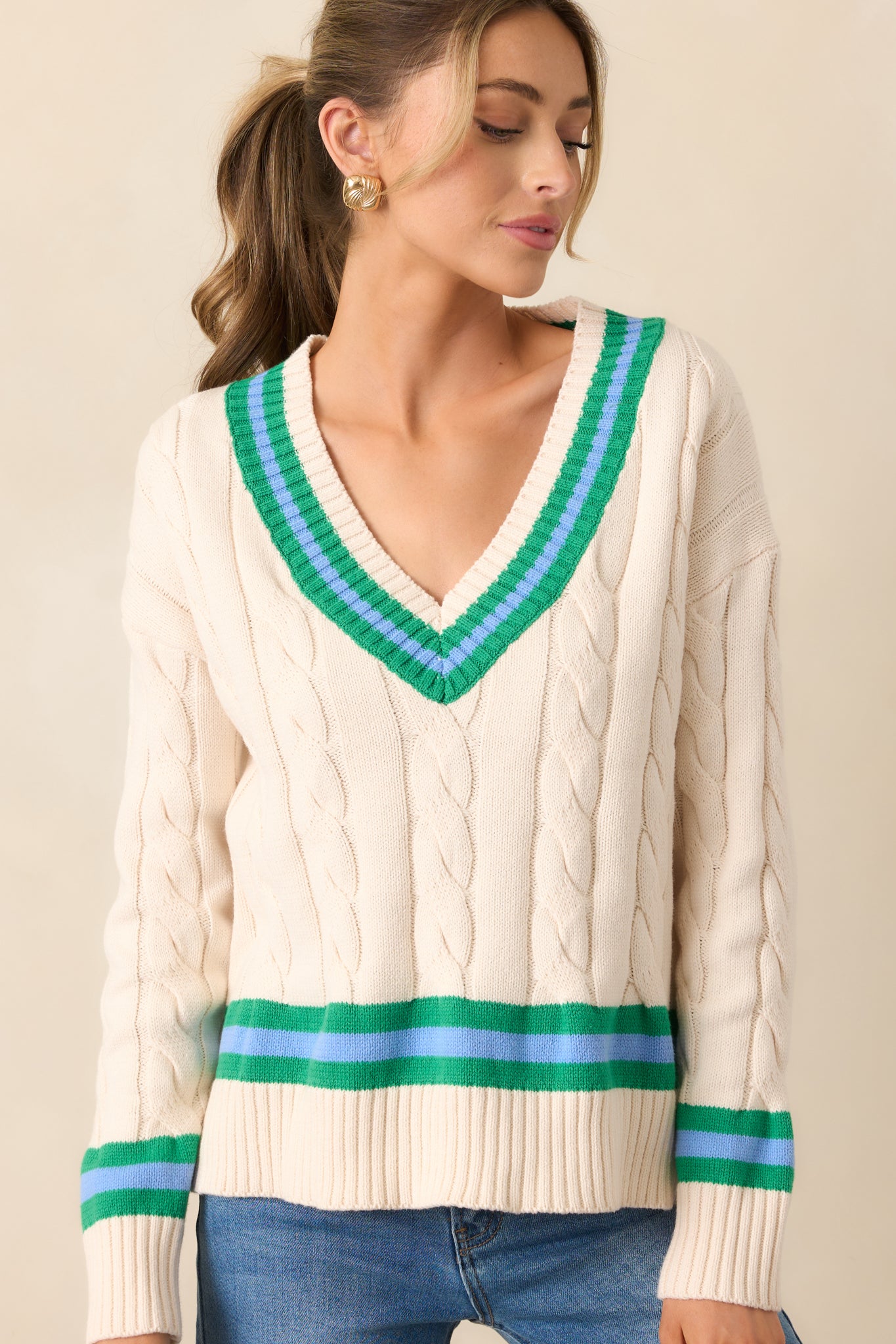 Detail of the long sleeves and split side hems of the ivory sweater, showcasing the oversized fit and green stripes that add a pop of color.