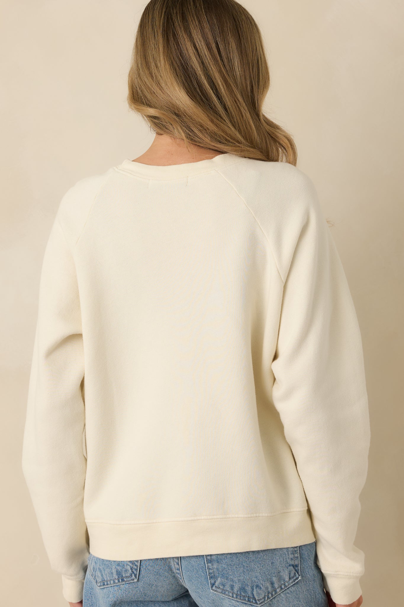 Rear view of ivory raglan sweatshirt highlighting plain back, ribbed hem, and raglan sleeve construction.