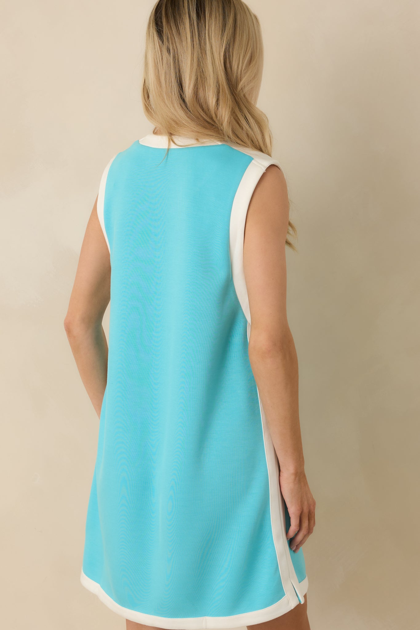 Rear view of the aqua mini dress showing sleeveless design, straight silhouette, and white trim along hem and side seams.