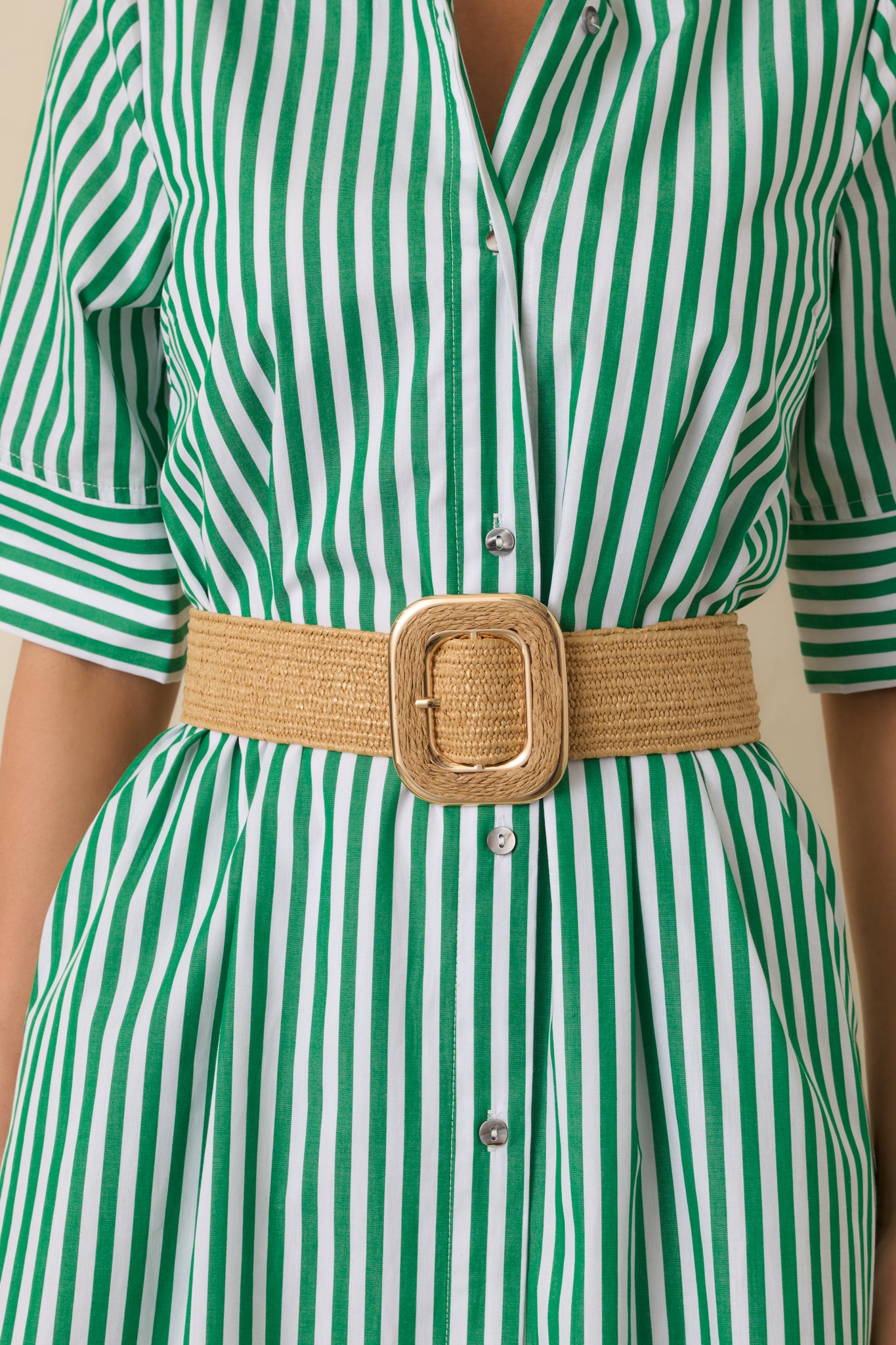 Cropped view of the tan woven belt highlighting the textured strap and square buckle in a matching tone.