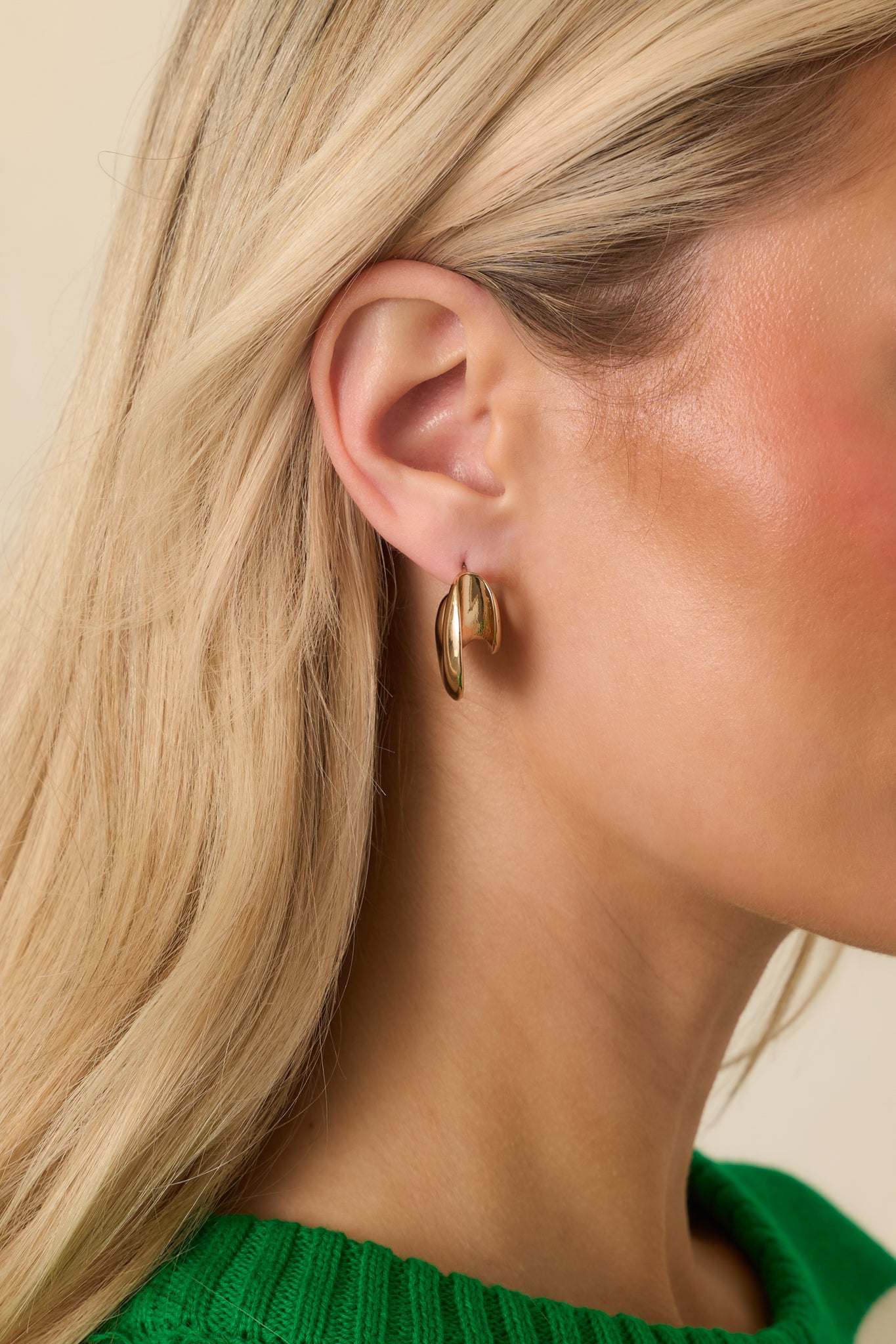 Gold earrings with a hollow sculptural design featuring an open C-hoop and secure post backings.