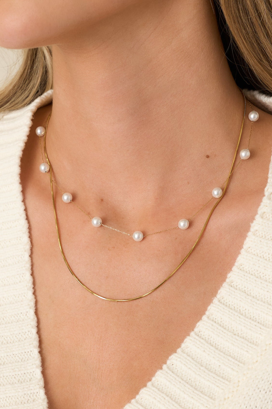Close view of the faux pearl accents and textured gold chains on the layered necklace.