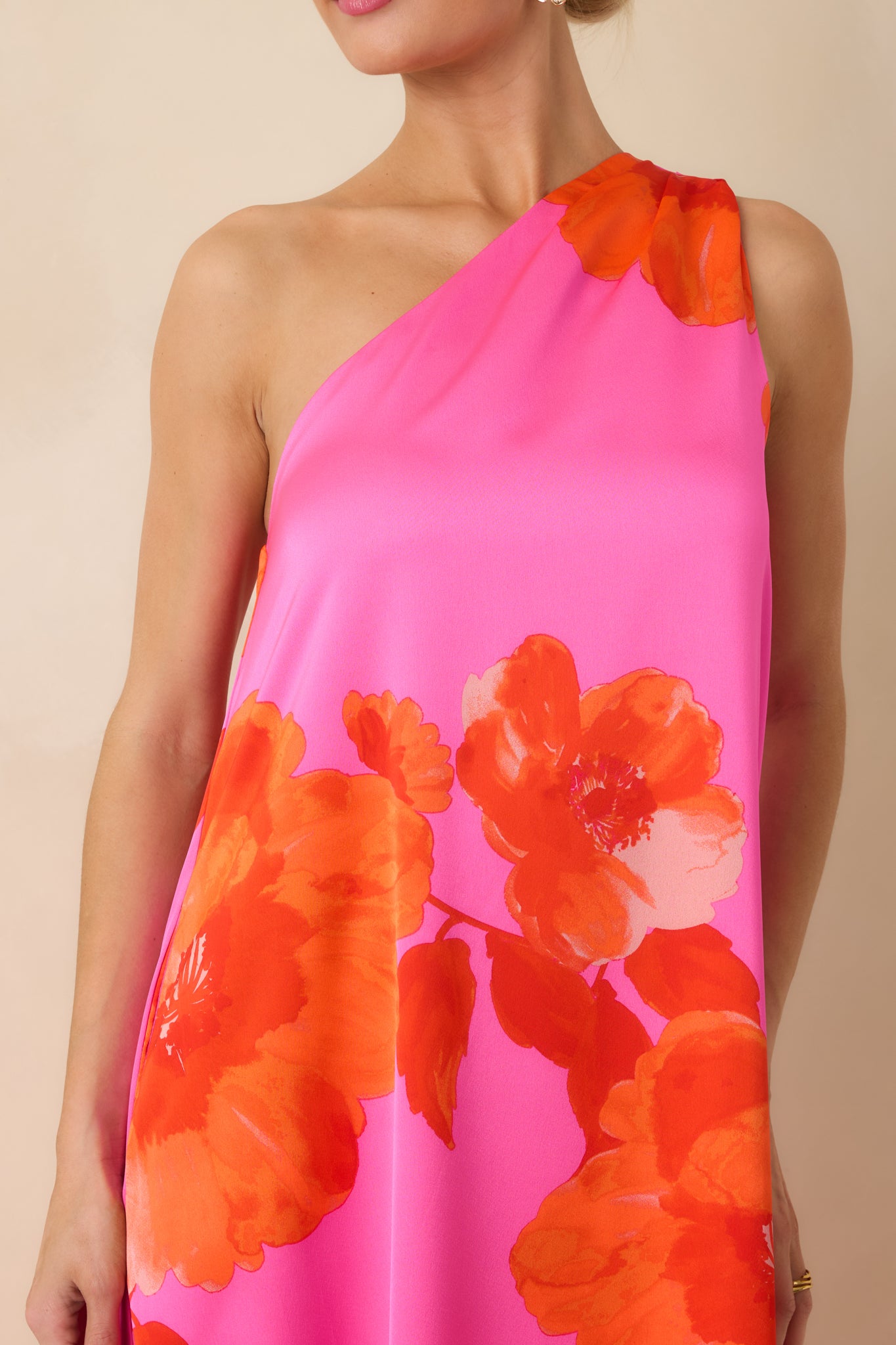 Close-up of the pink satin fabric with red floral print, showing the draped one-shoulder design and smooth texture.
