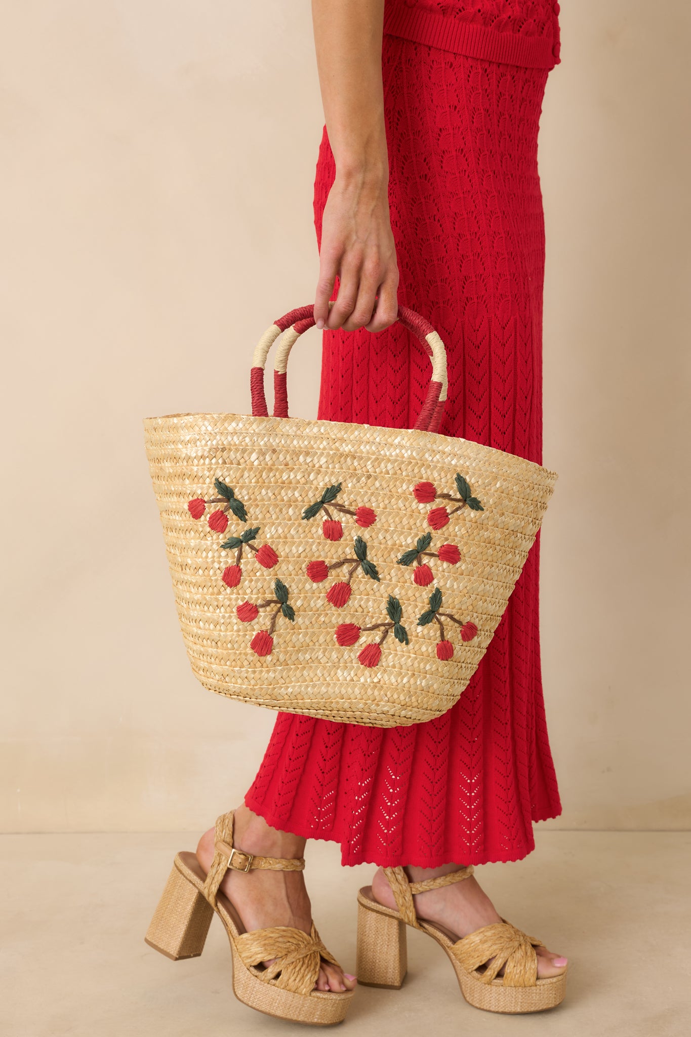 Front view of the natural woven straw tote bag showcasing embroidered cherry detailing and dual top handles with red and ivory accents.