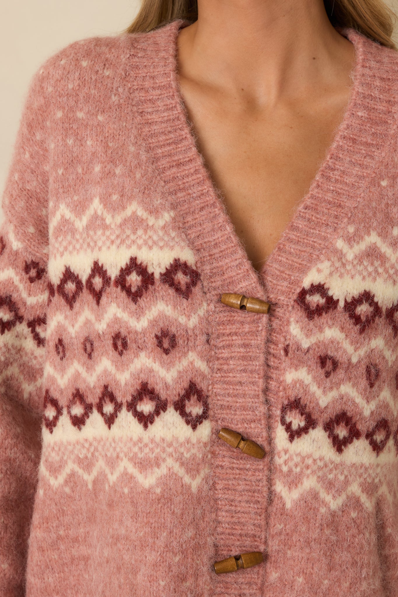 Close-up of rose pink cardigan showing wooden toggle buttons, Fair Isle pattern, and knit texture.