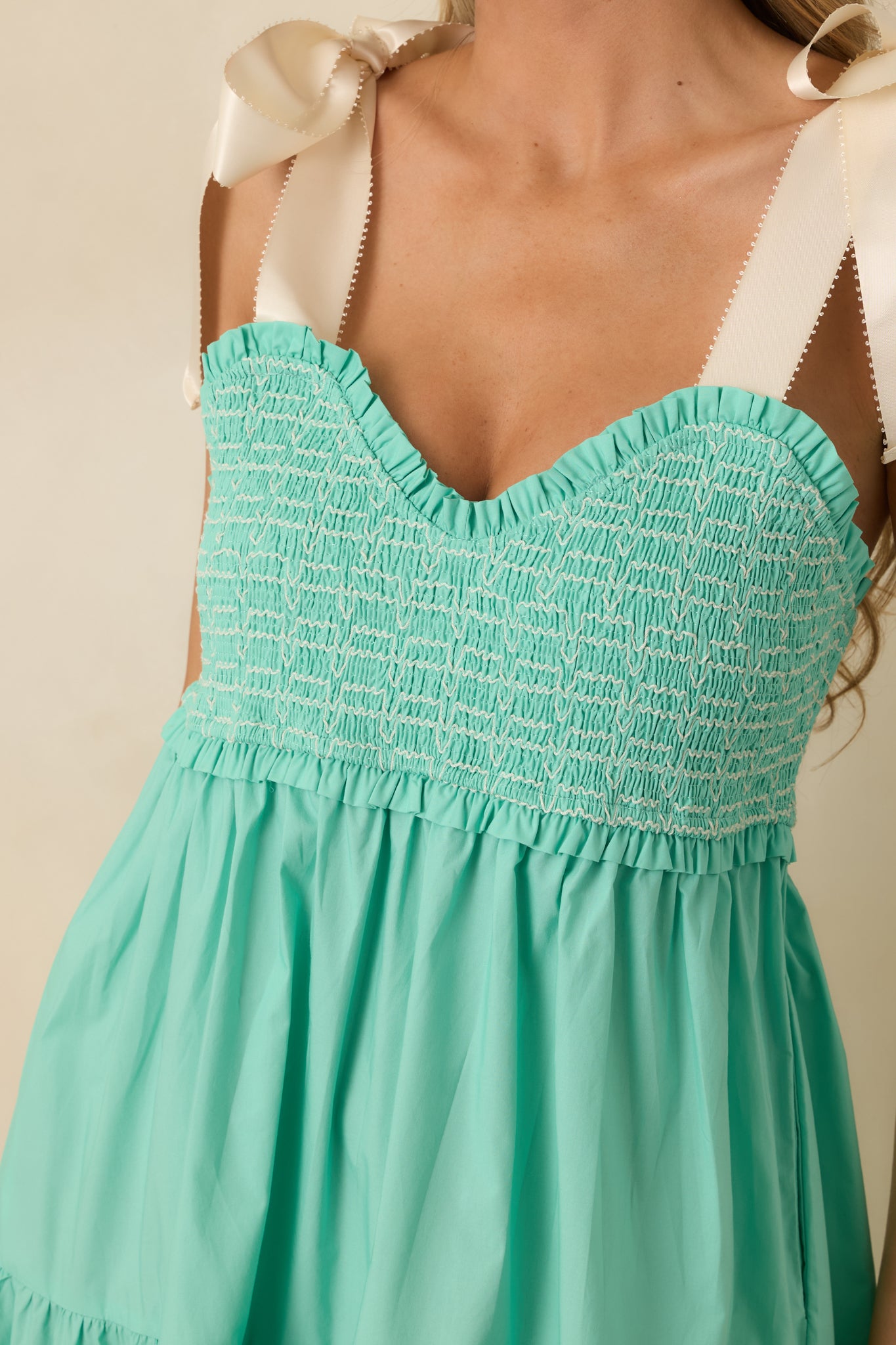 Close-up of mint green midi dress showing white embroidered smocking and ivory self-tie bow straps.