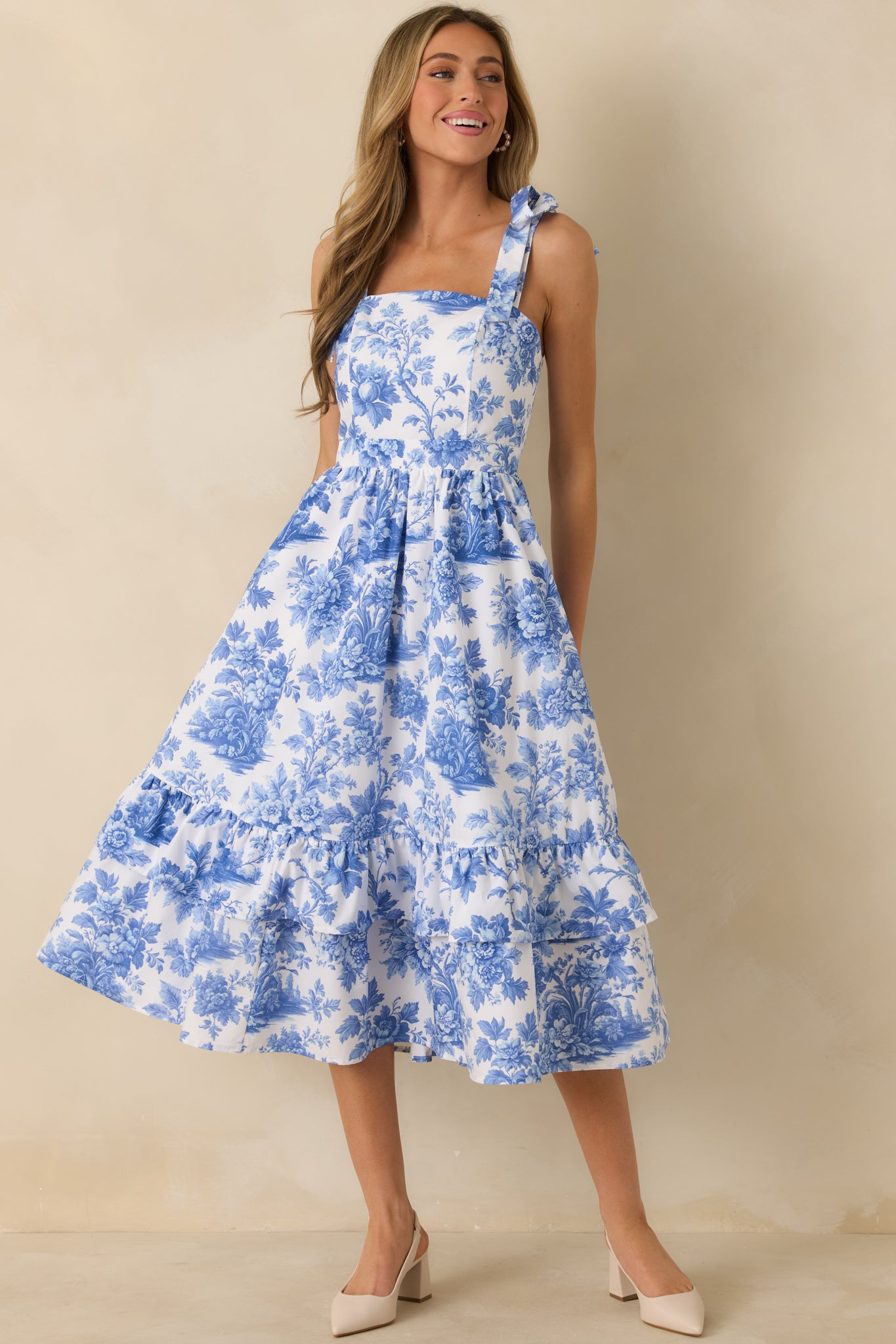 Blue and white cotton midi dress with an allover floral print, square neckline, and bow-tied shoulder straps, finished with a tiered skirt.