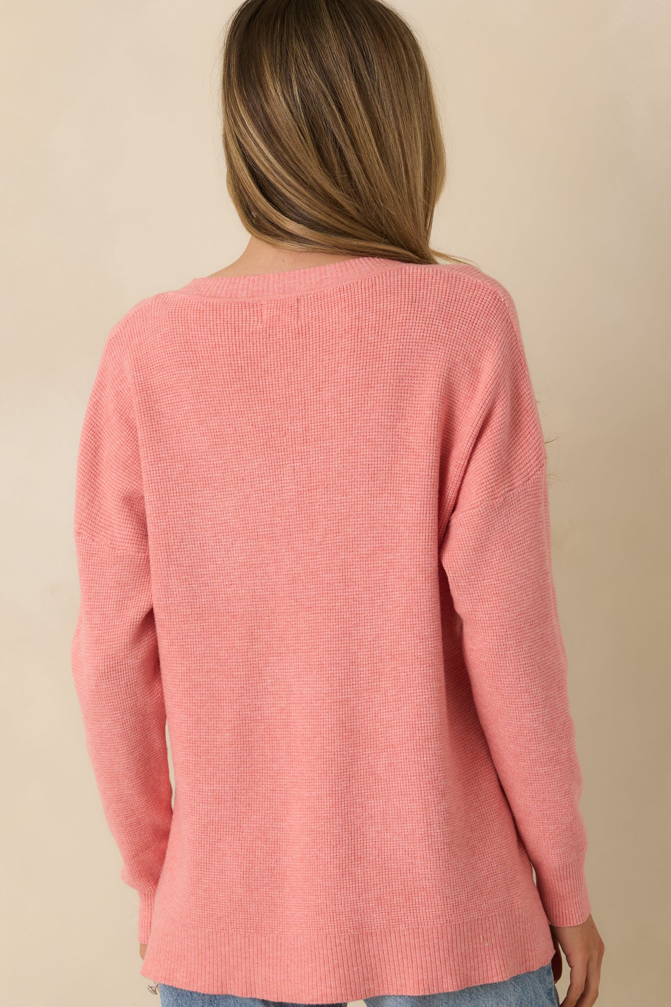 Rear view of rose sweater highlighting relaxed fit, long sleeves, and split hem bottom.