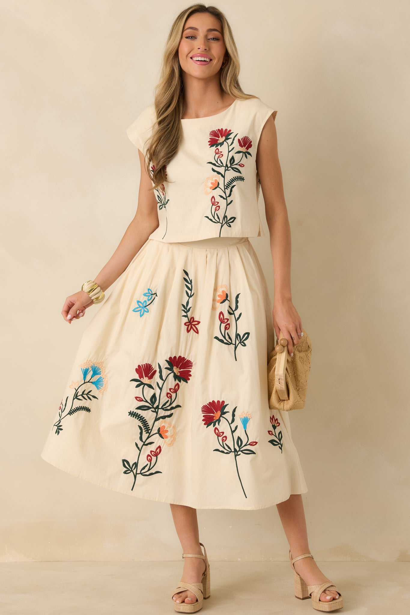 Natural-colored top with floral embroidery across the front, bateau neckline, and cap sleeves in a structured silhouette.