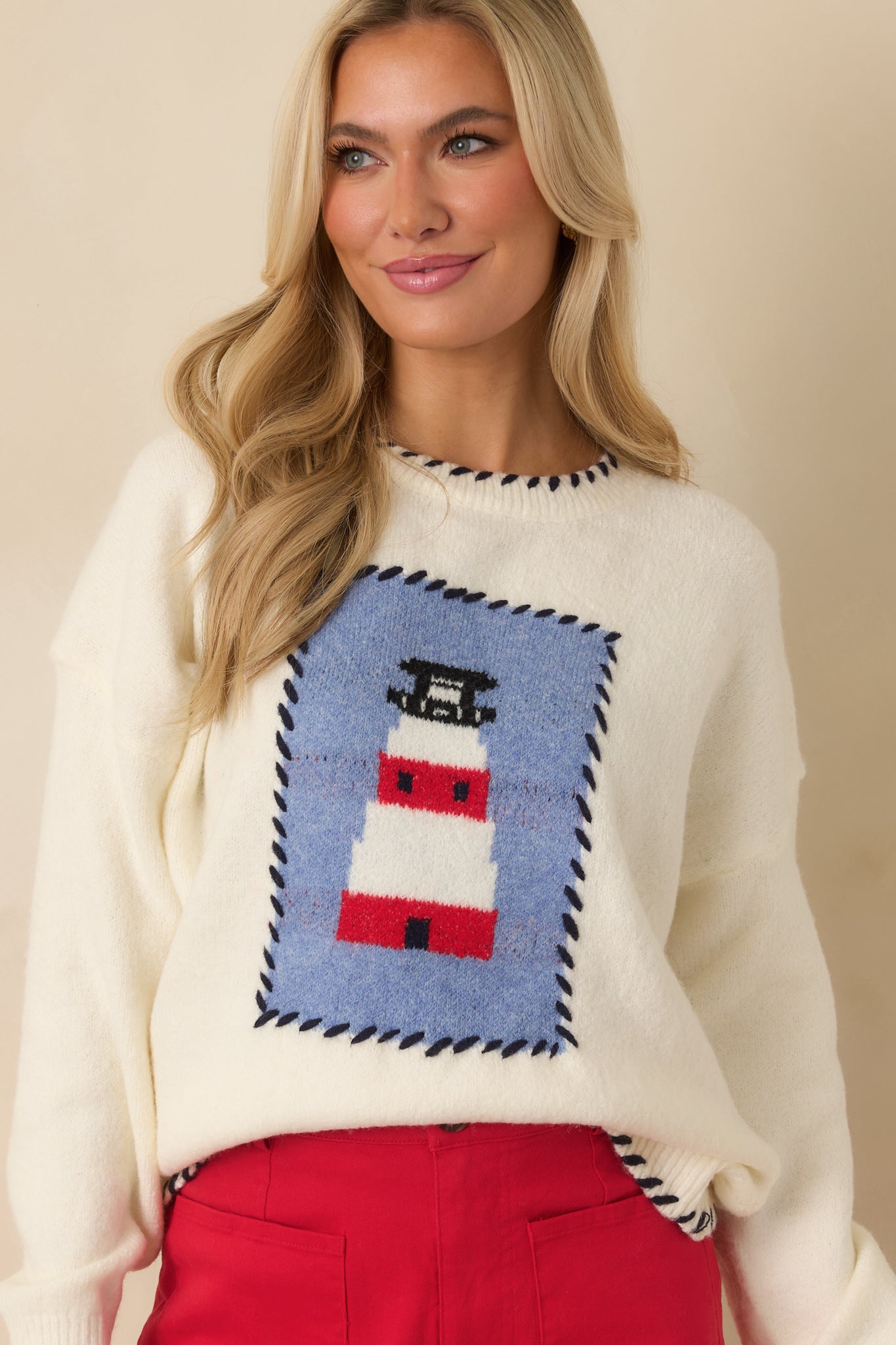 Cropped detail of the ivory sweater emphasizing the lighthouse design and contrast whipstitch stitching along the neckline.