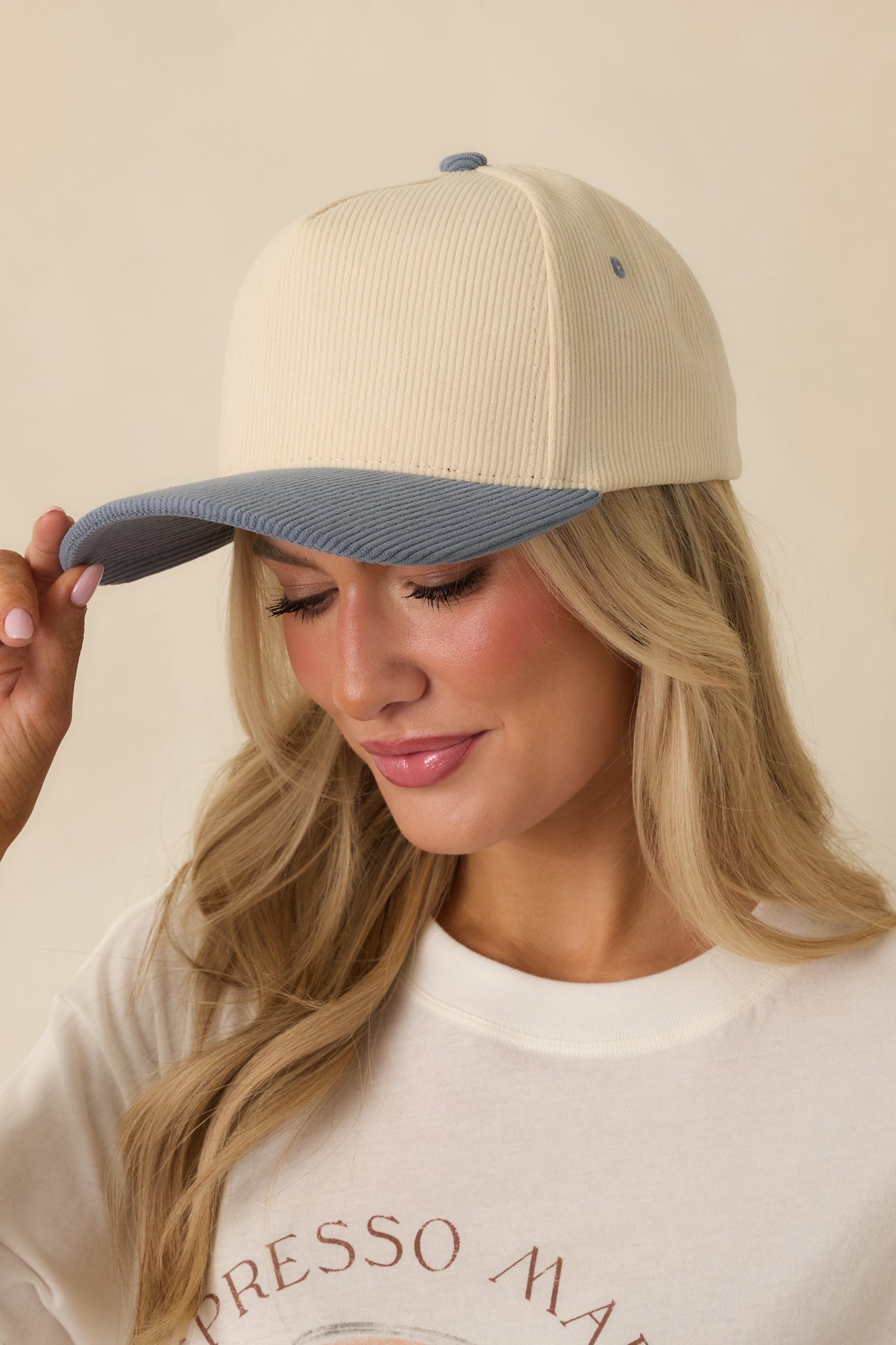 Close-up of ivory cap showing blue top button, vent hole stitching, and smooth fabric texture.