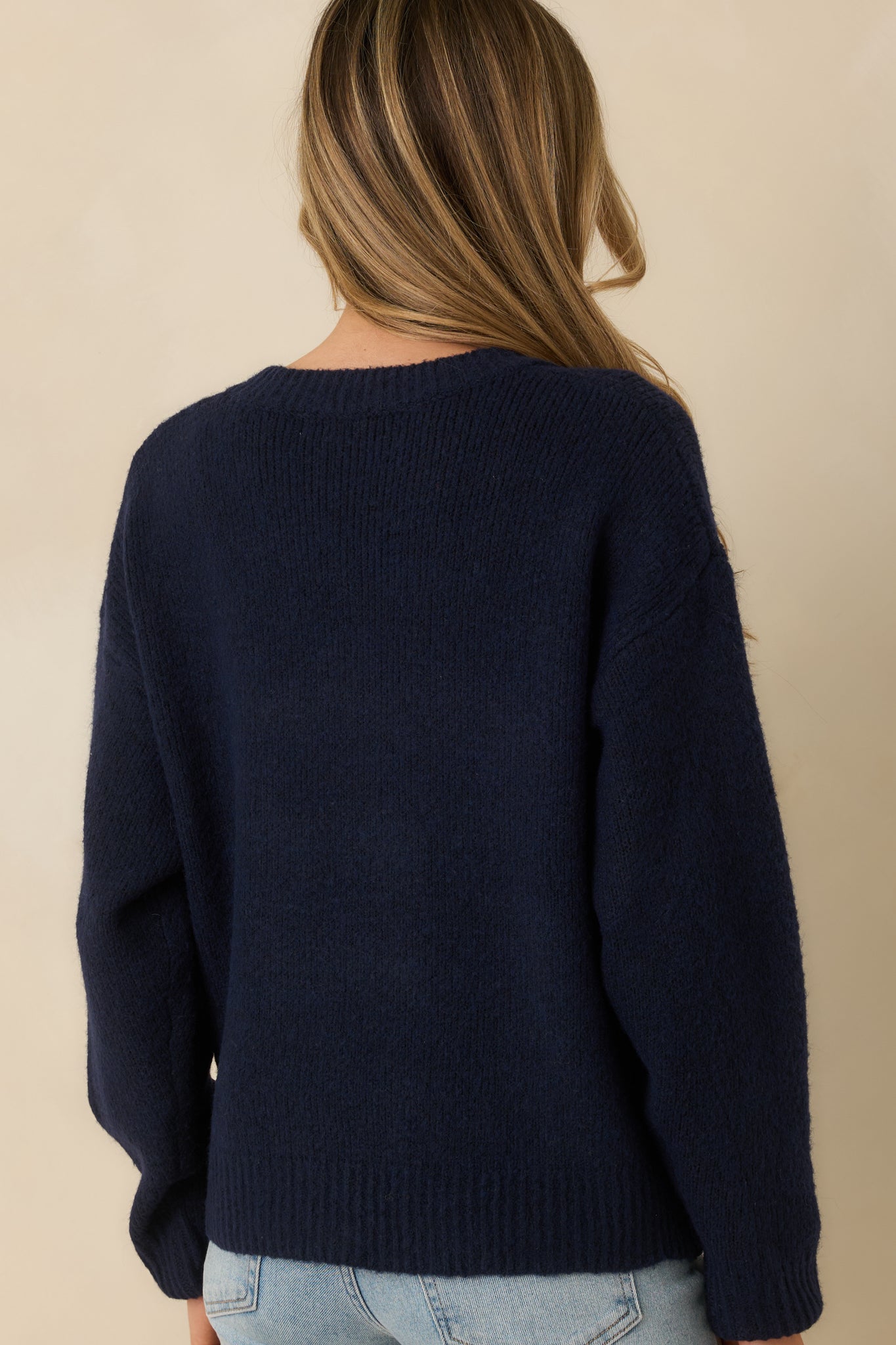 Navy knit sweater displaying the relaxed silhouette from the rear with ribbed trim along hem and cuffs and embroidered detailing.