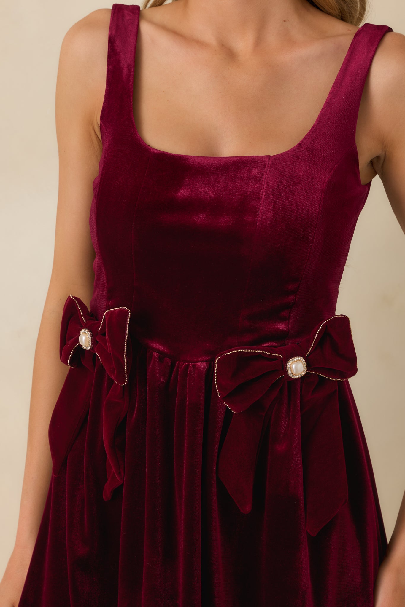 Close-up of the velvet fabric, decorative bow, and faux pearl accents at the waist of the burgundy mini dress.