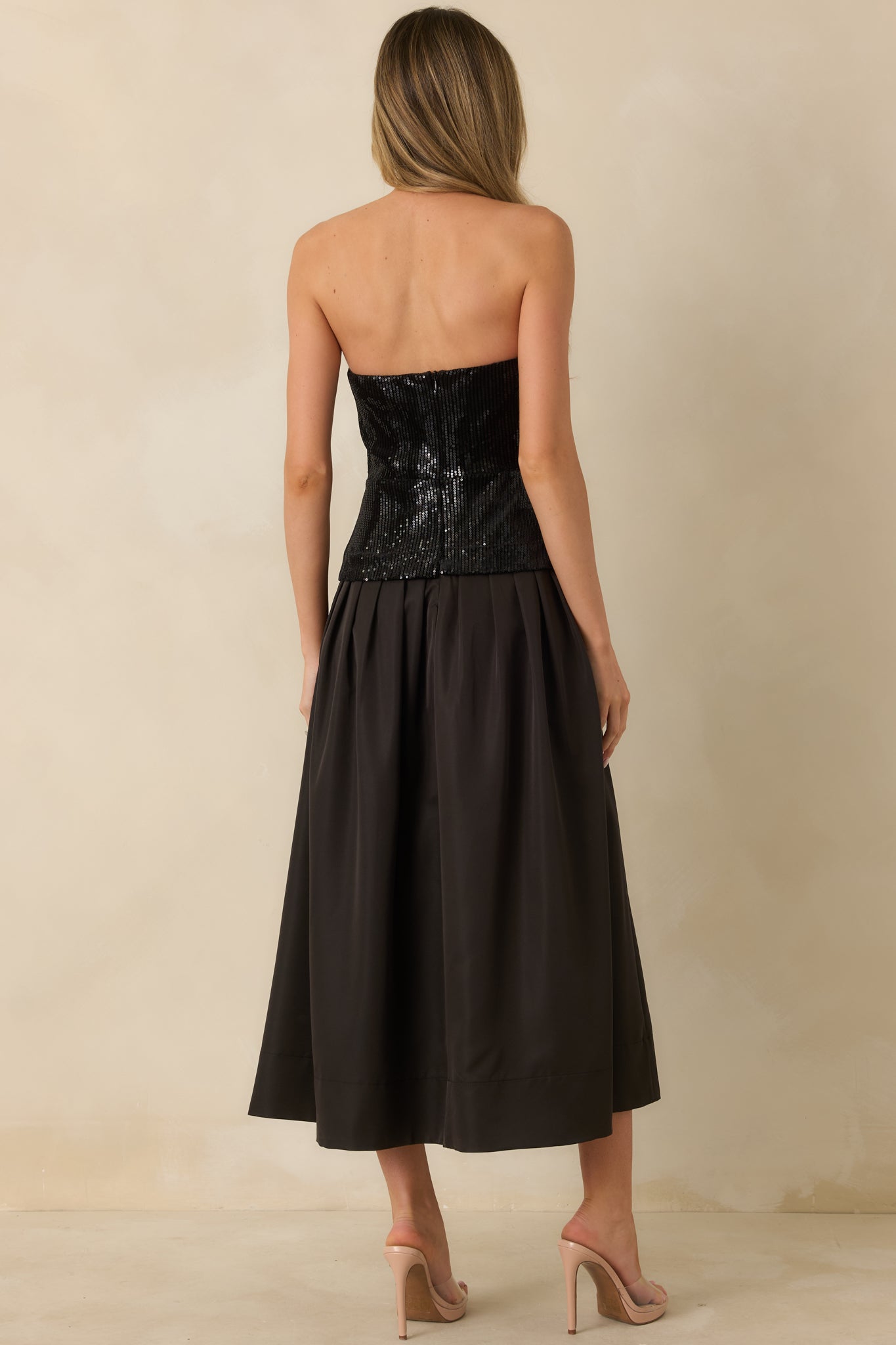 Rear view of the black midi dress showing the strapless sequin bodice with back zipper closure and the pleated skirt flowing from the waist.