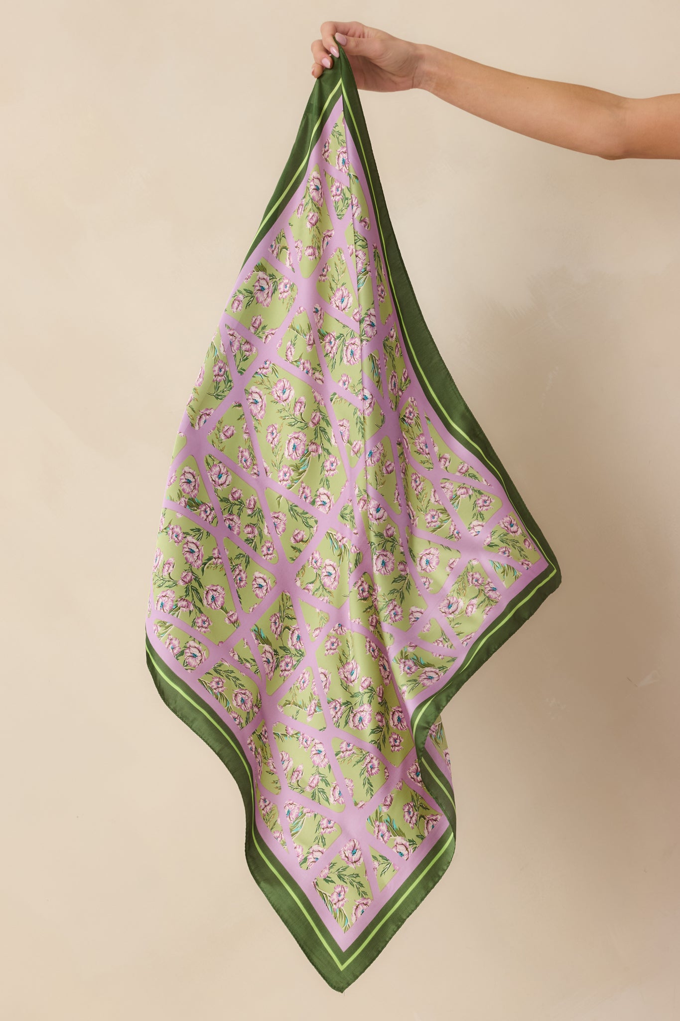 Model holding floral and geometric patterned green scarf showing lavender blossoms over a lavender lattice design on a soft green background.