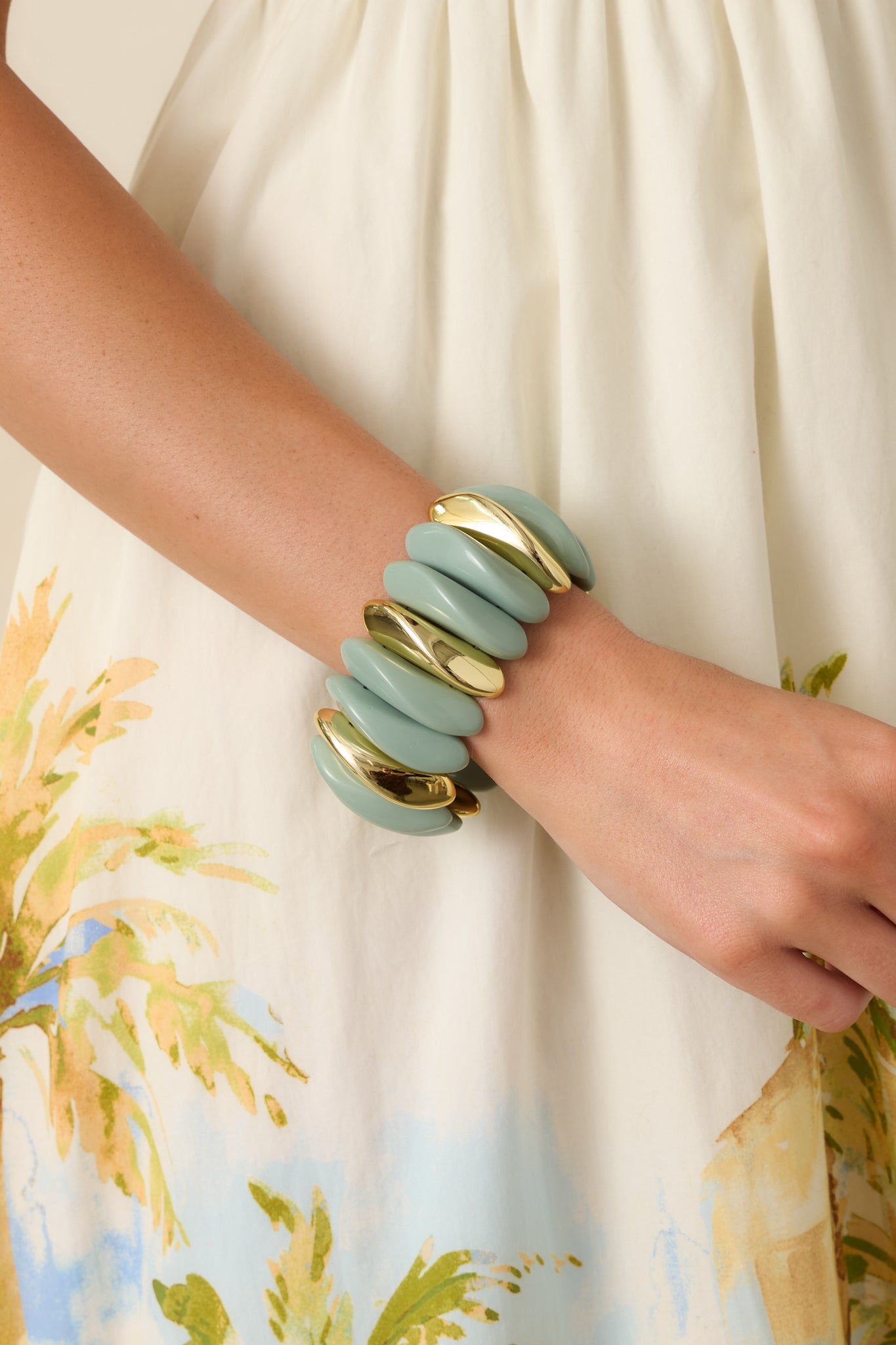 Detailed close-up of the contoured sage green links and gold accent pieces on the flexible elastic band.