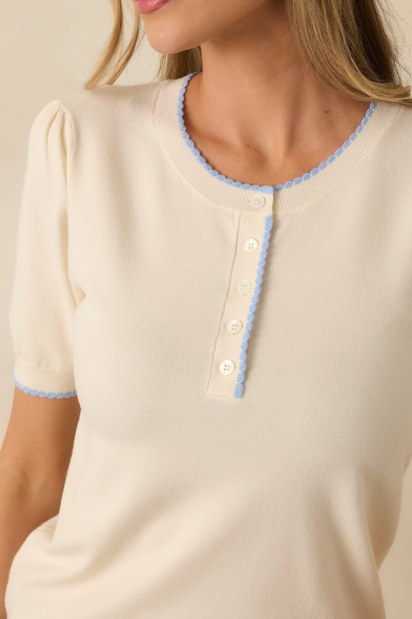 Close-up of the ivory sweater showing the round neckline, partial button placket, and soft knit texture.