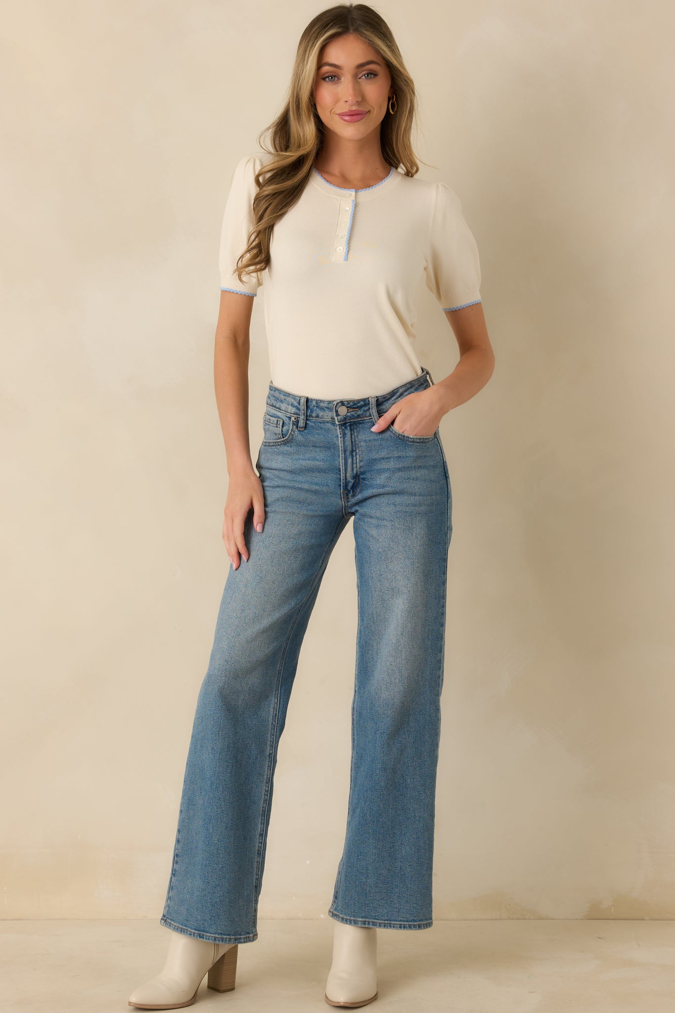 Front view of an ivory knit sweater with a round neckline, blue contrast trim, short gathered sleeves, and straight hem.