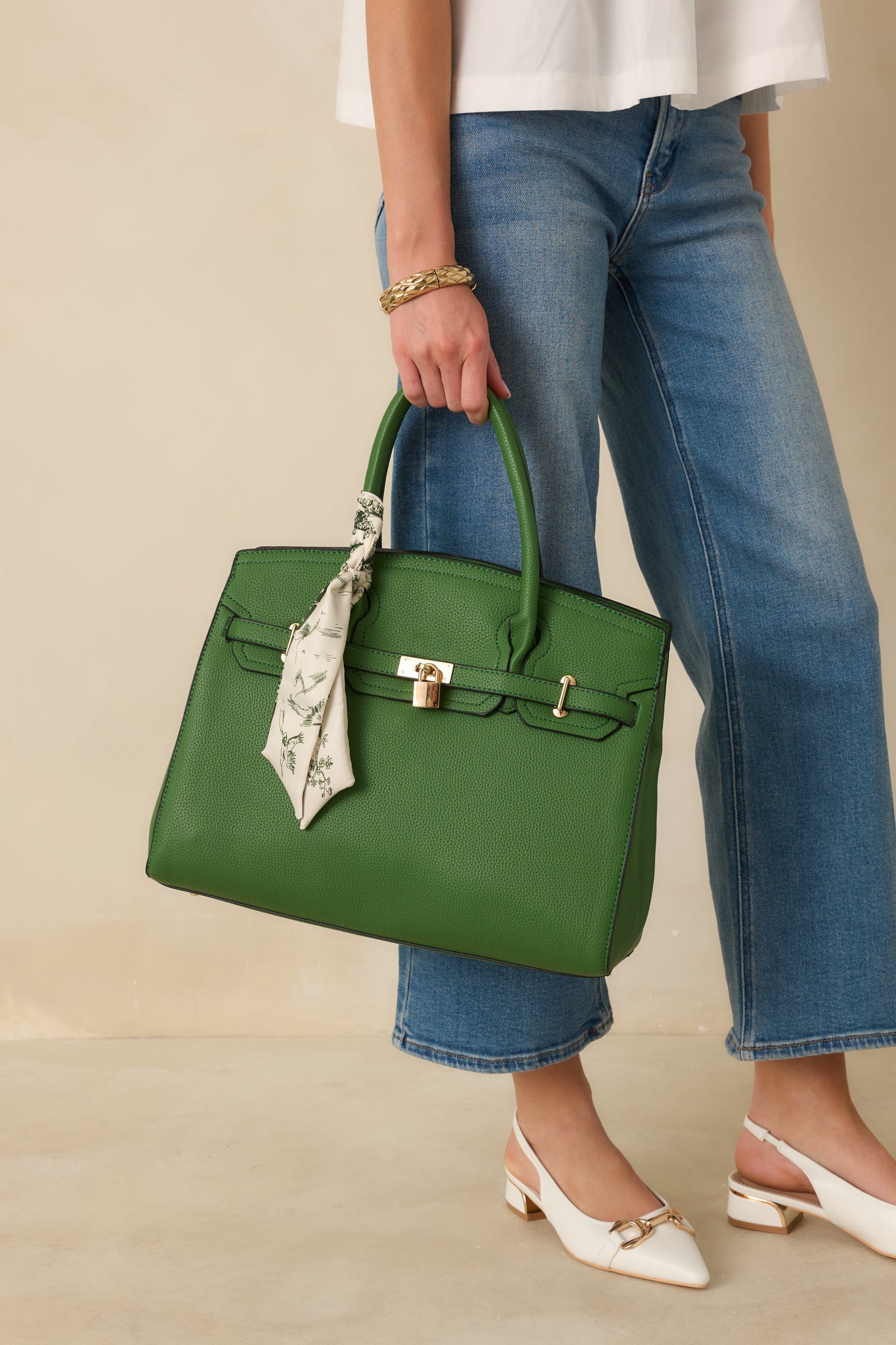 Front view of green handbag showing two top handles, removable shoulder strap, and decorative beige and green scarf.