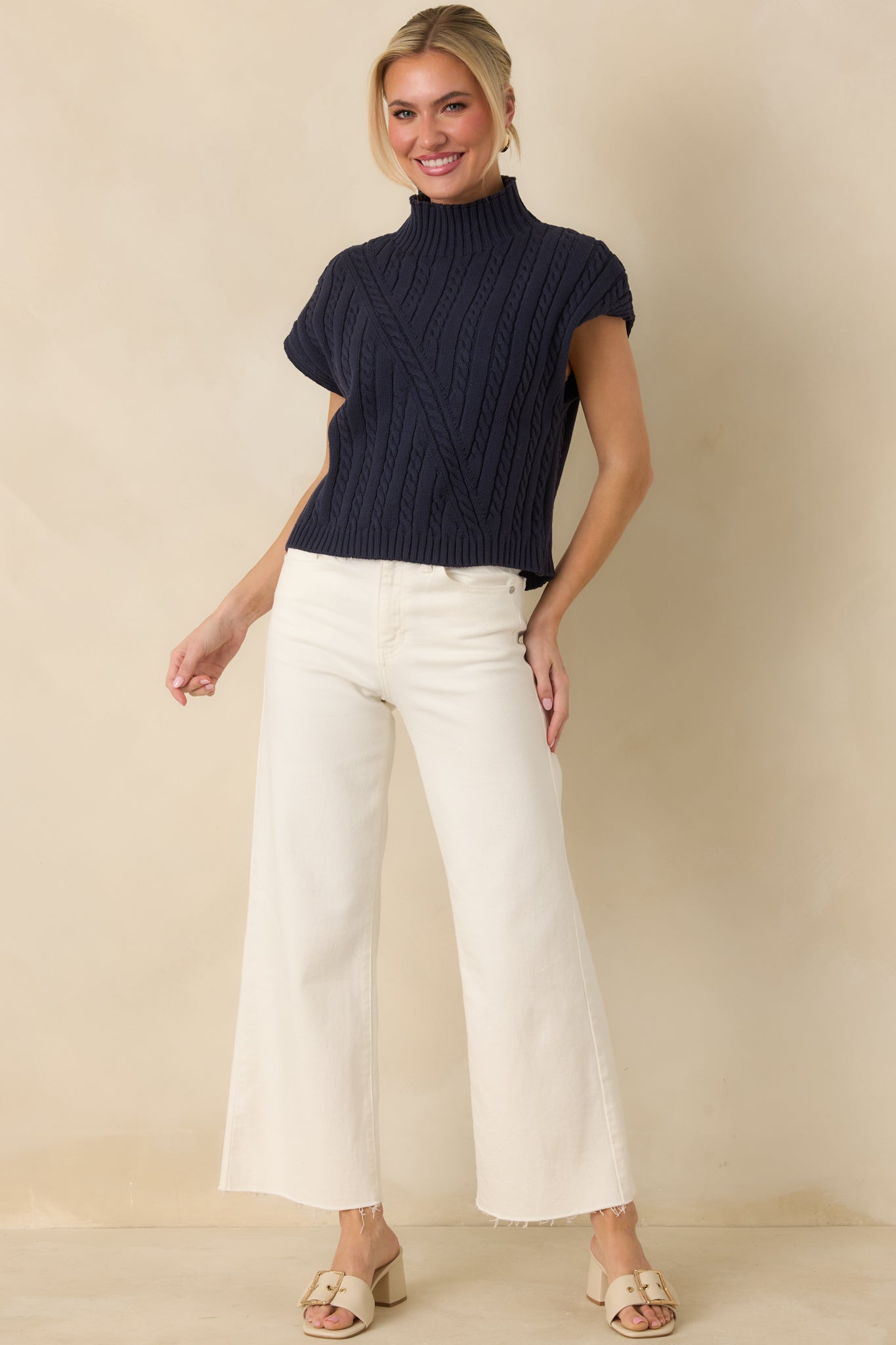 Cable knit navy top designed with a sleeveless shape, polished mock neck, and clean ribbed trim along the hem.
