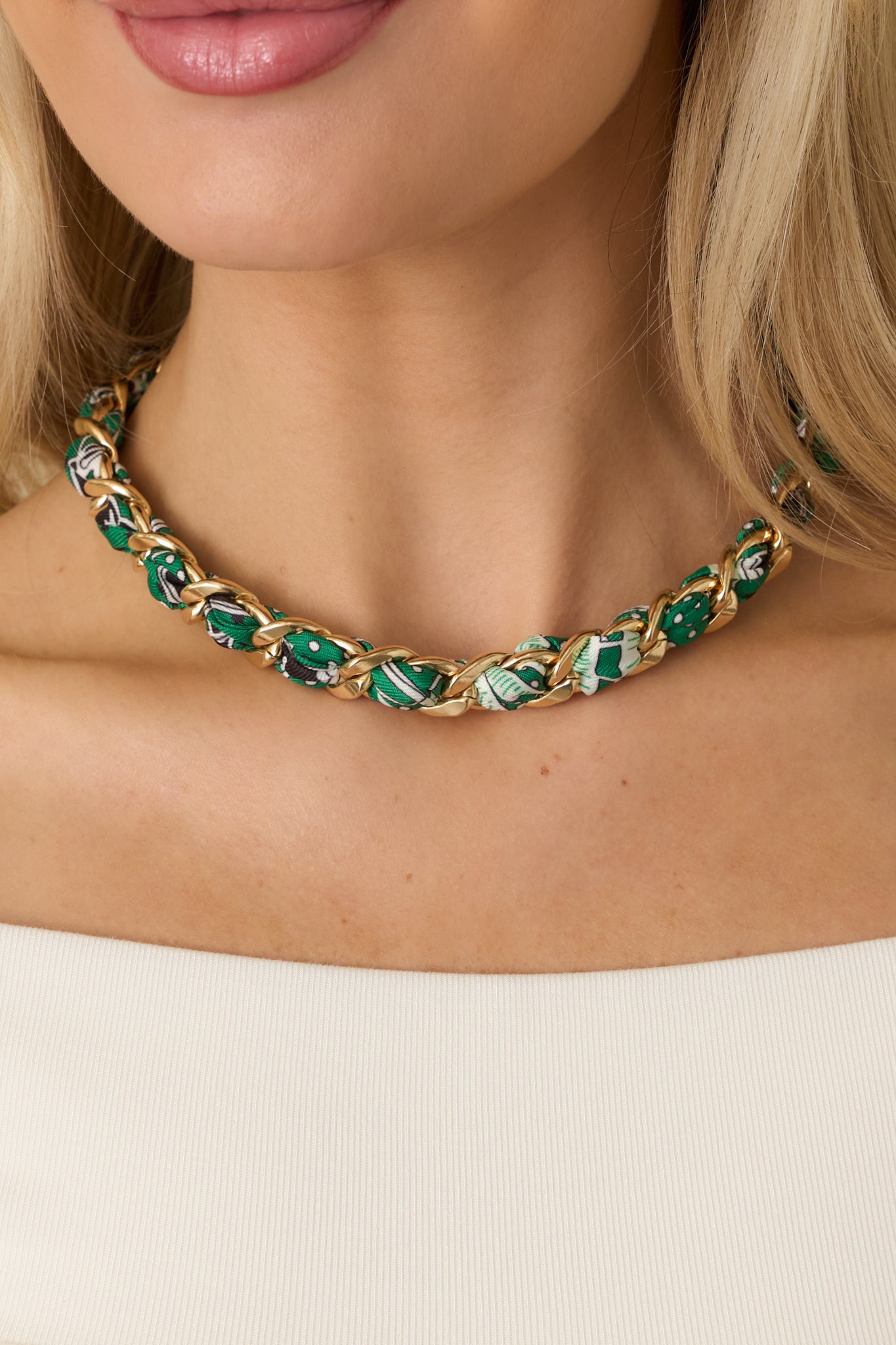 Close-up of polished gold links interlaced with green multi-patterned fabric emphasizing texture, dimension, and clasp hardware.