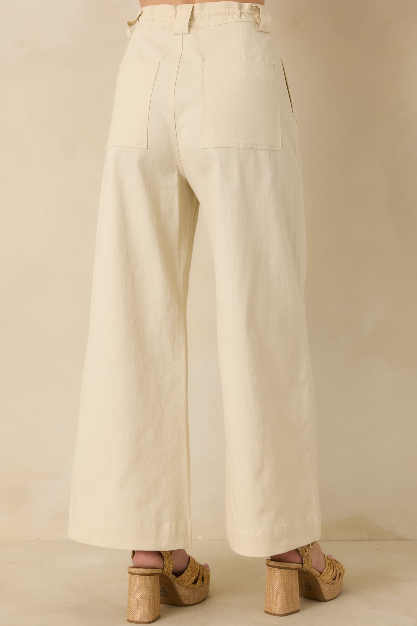 Back view of the beige wide-leg pants displaying the smooth back waistband and relaxed leg silhouette.