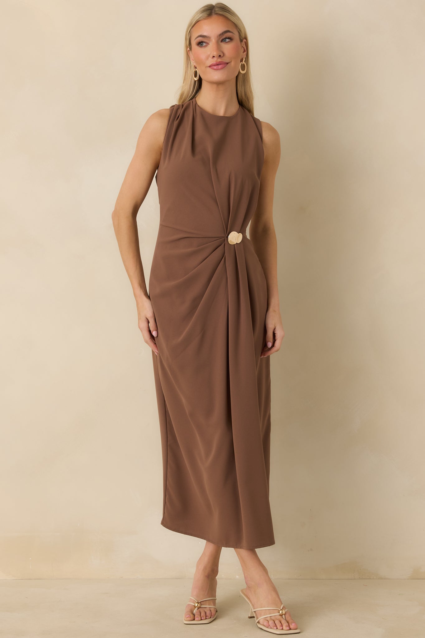 Light brown sleeveless dress with round neckline and ruched front detail accented by gold embellishment.