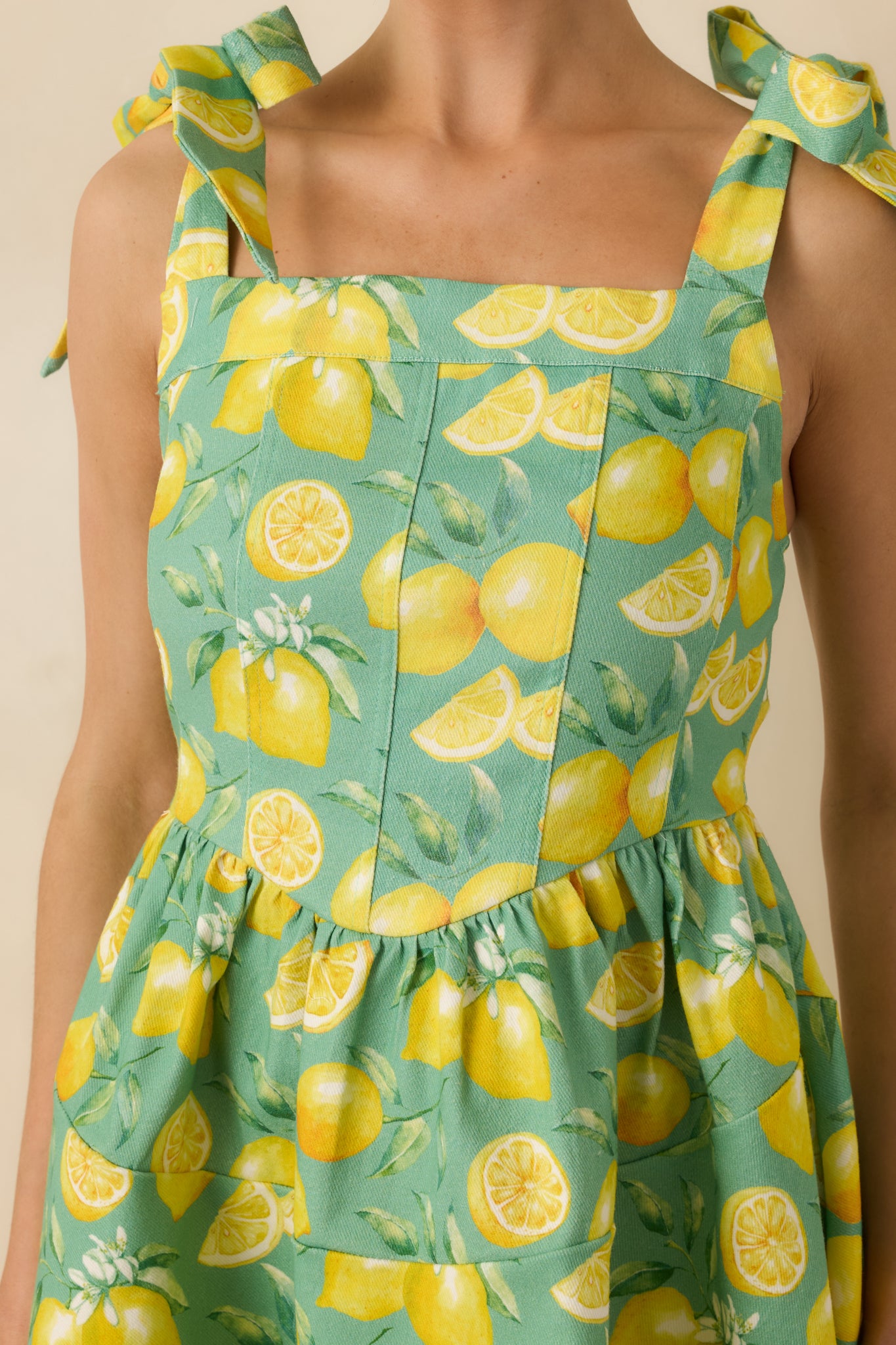 Close-up of green mini dress showing the lemon print, fabric texture, and bow strap detail.