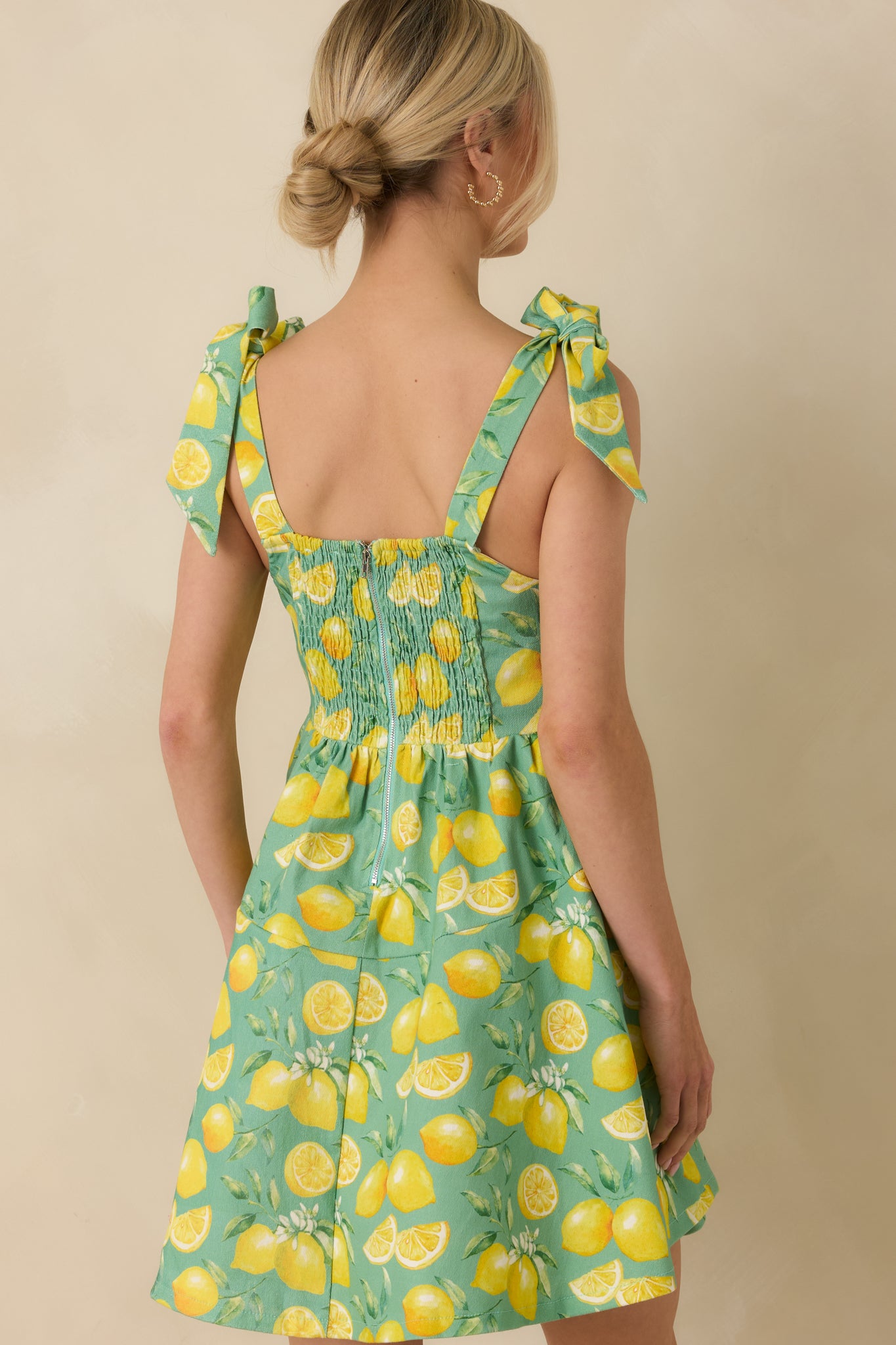 Back view of green mini dress highlighting the smocked back panel, adjustable straps, and zipper closure.