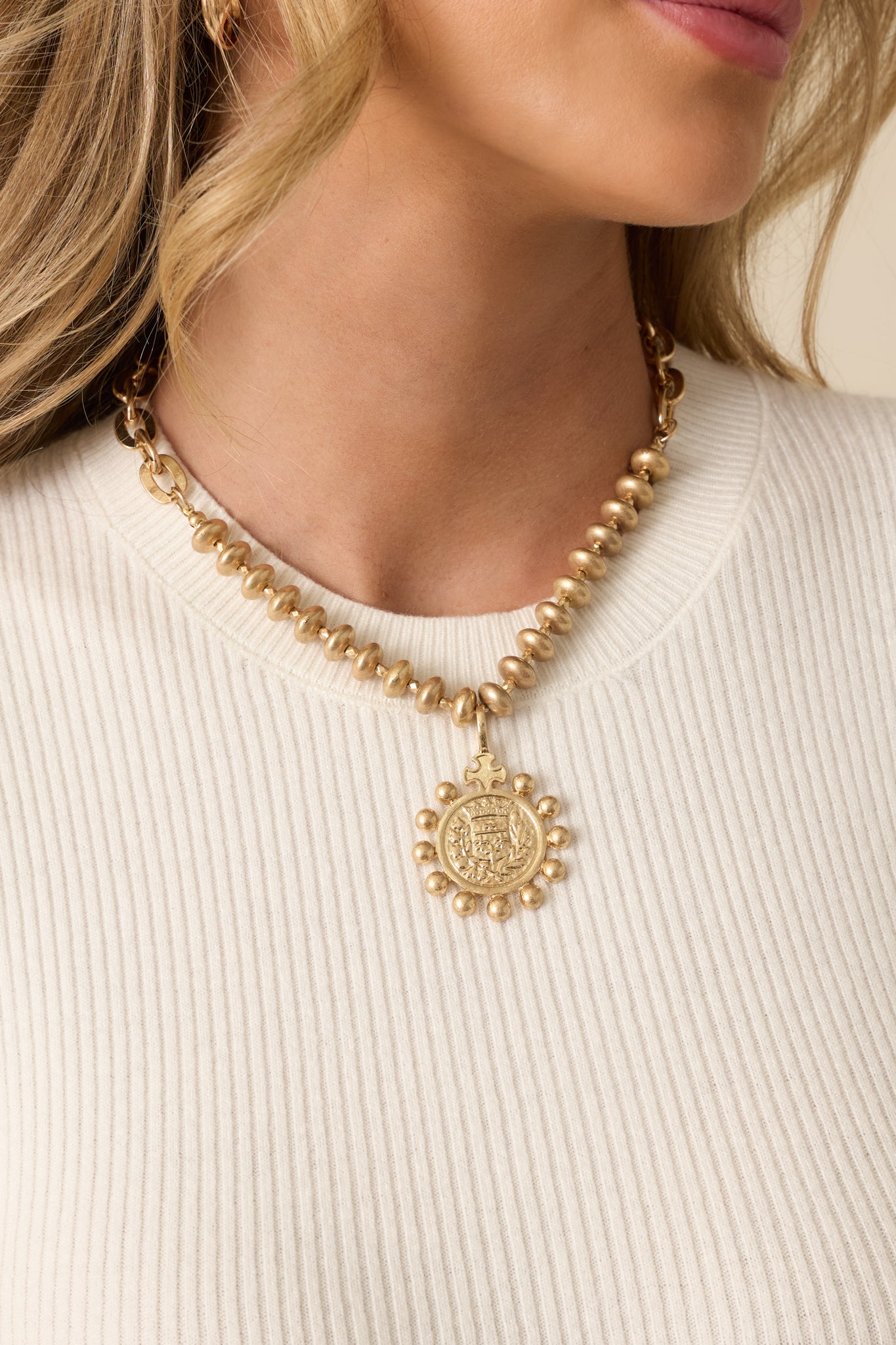Worn gold necklace featuring stacked disc beads, a chunky chain, and a large embossed crest medallion pendant shown from the front.