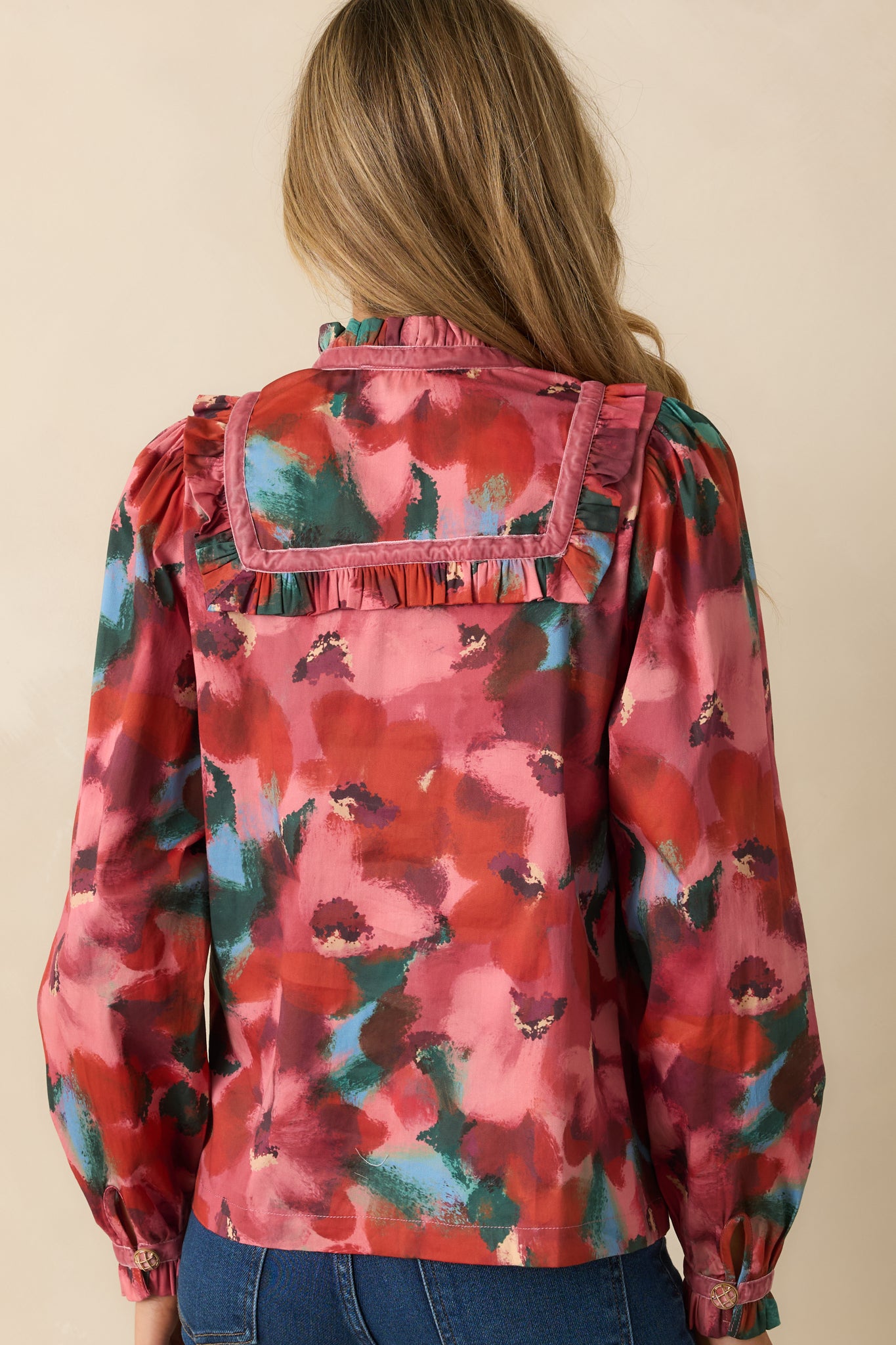 Rear view of the pink top showing the abstract floral print, straight hem, and puff sleeves with buttoned ruffle cuffs from behind.