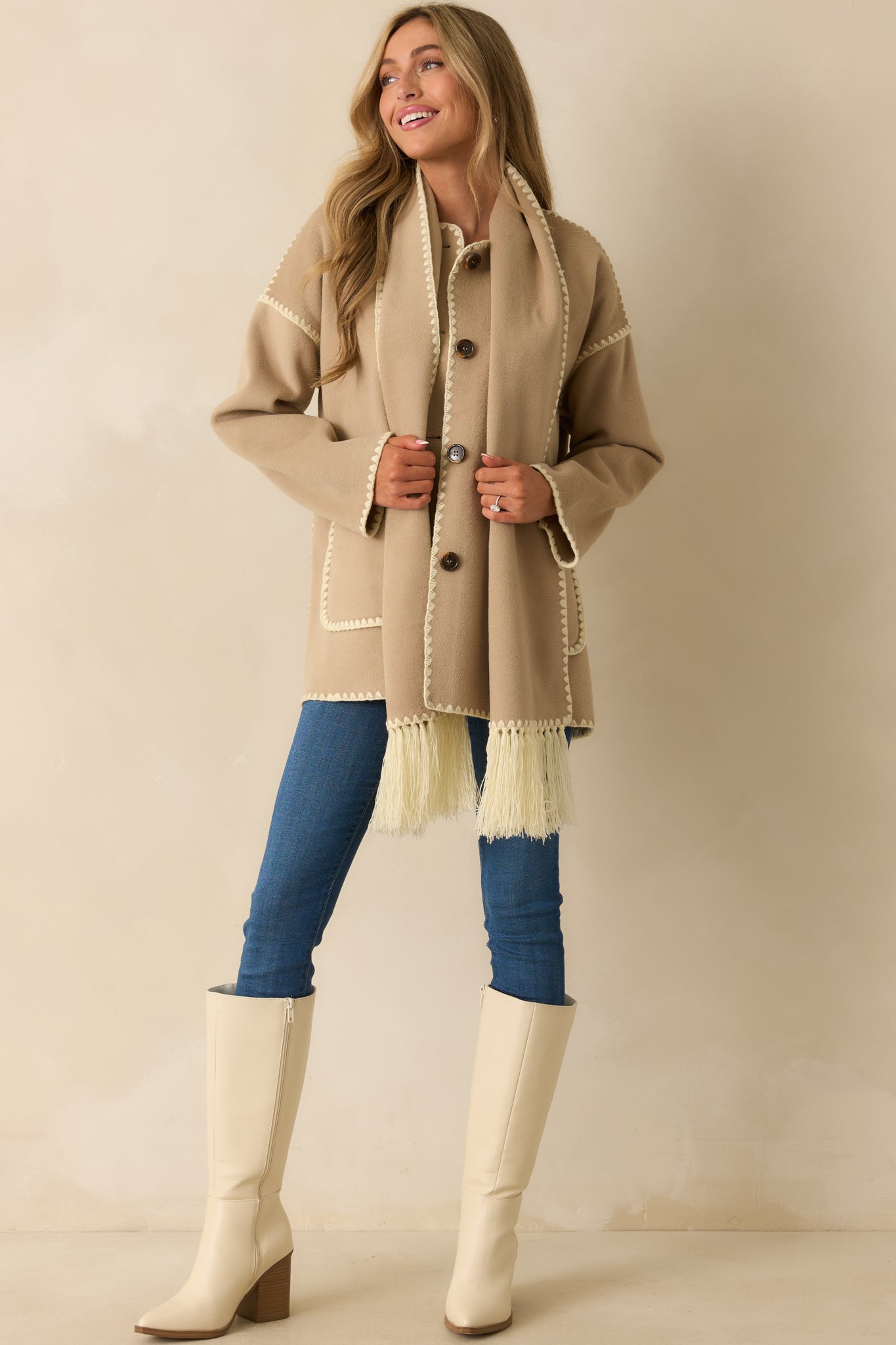 Front view of the taupe coat showing the rounded neckline, button closure, and long sleeves with blanket stitch detailing.