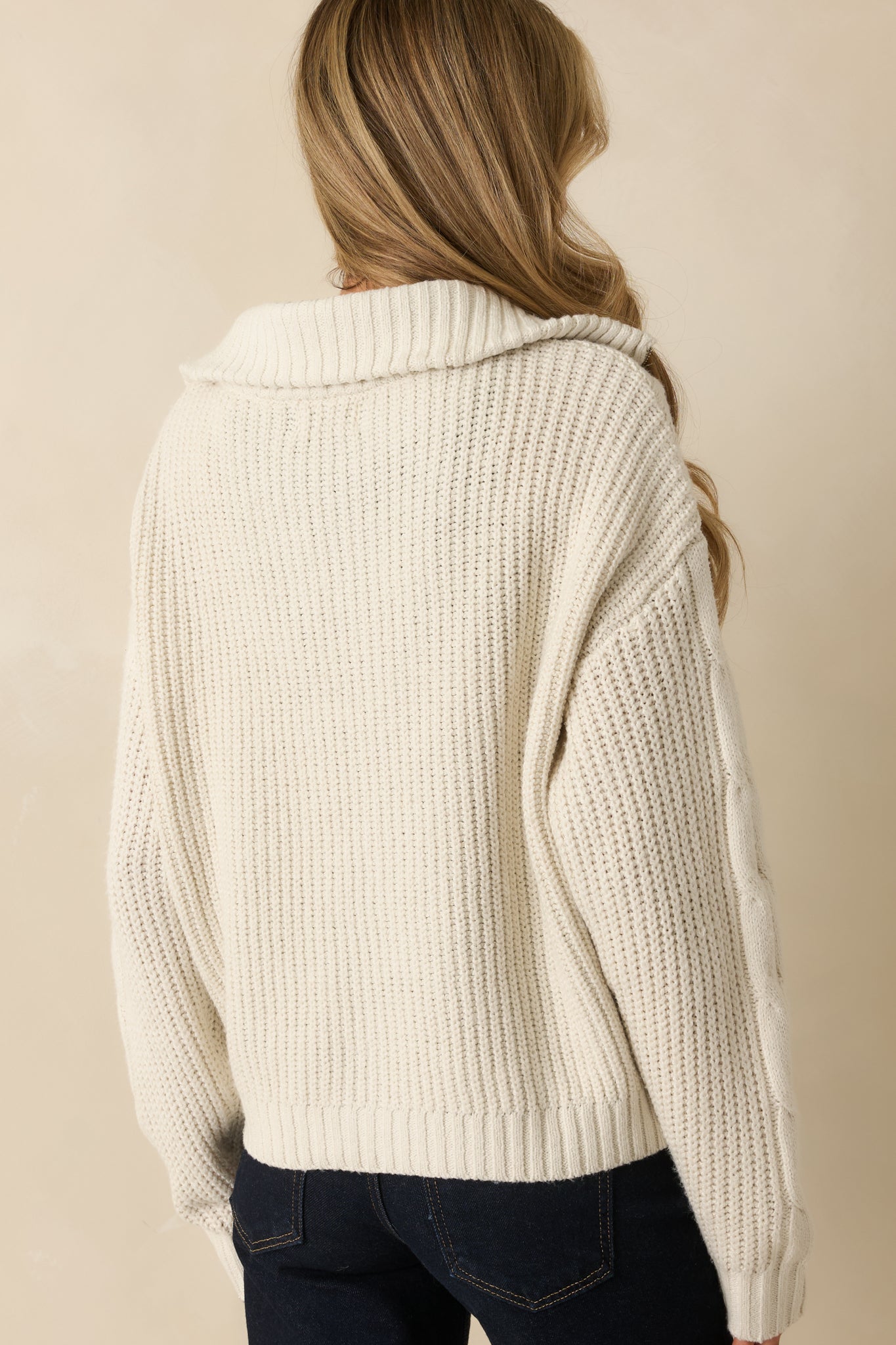 Back view of the ivory jacket highlighting the fold-over collar, long sleeves, and ribbed hem at the bottom.