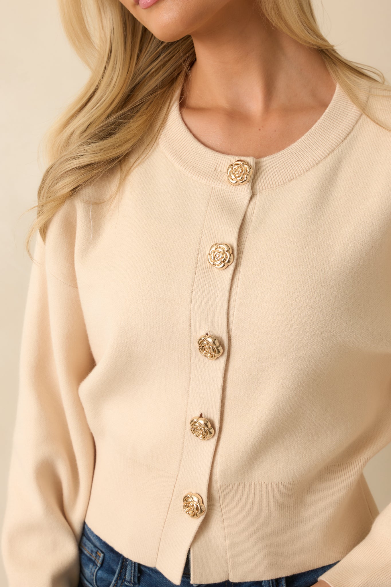 Detailed view of the gold flower-shaped button, ribbed hems, and knit texture.