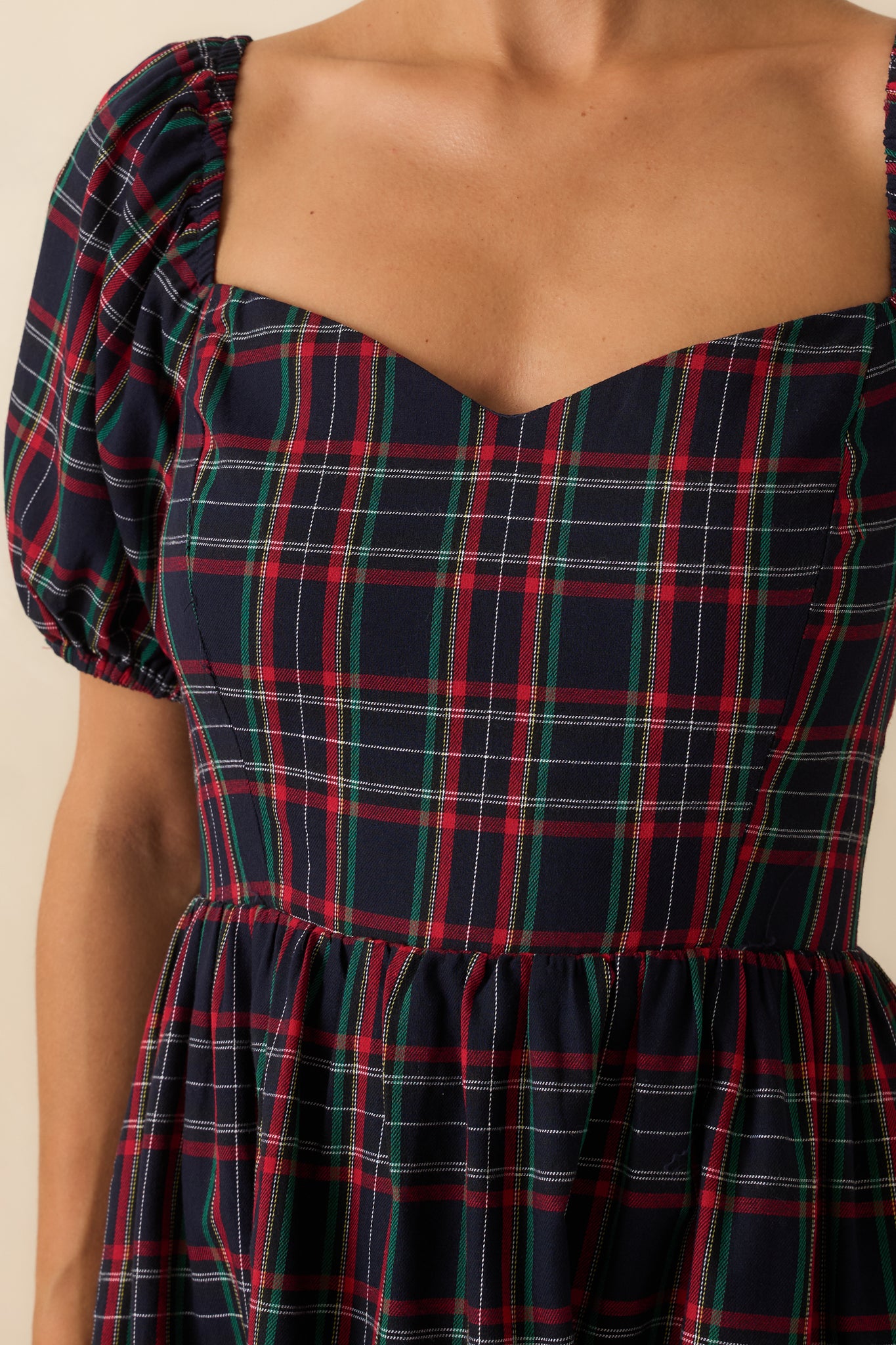 Macro view of the plaid fabric, sweetheart neckline, and puff sleeve detailing on the navy dress.