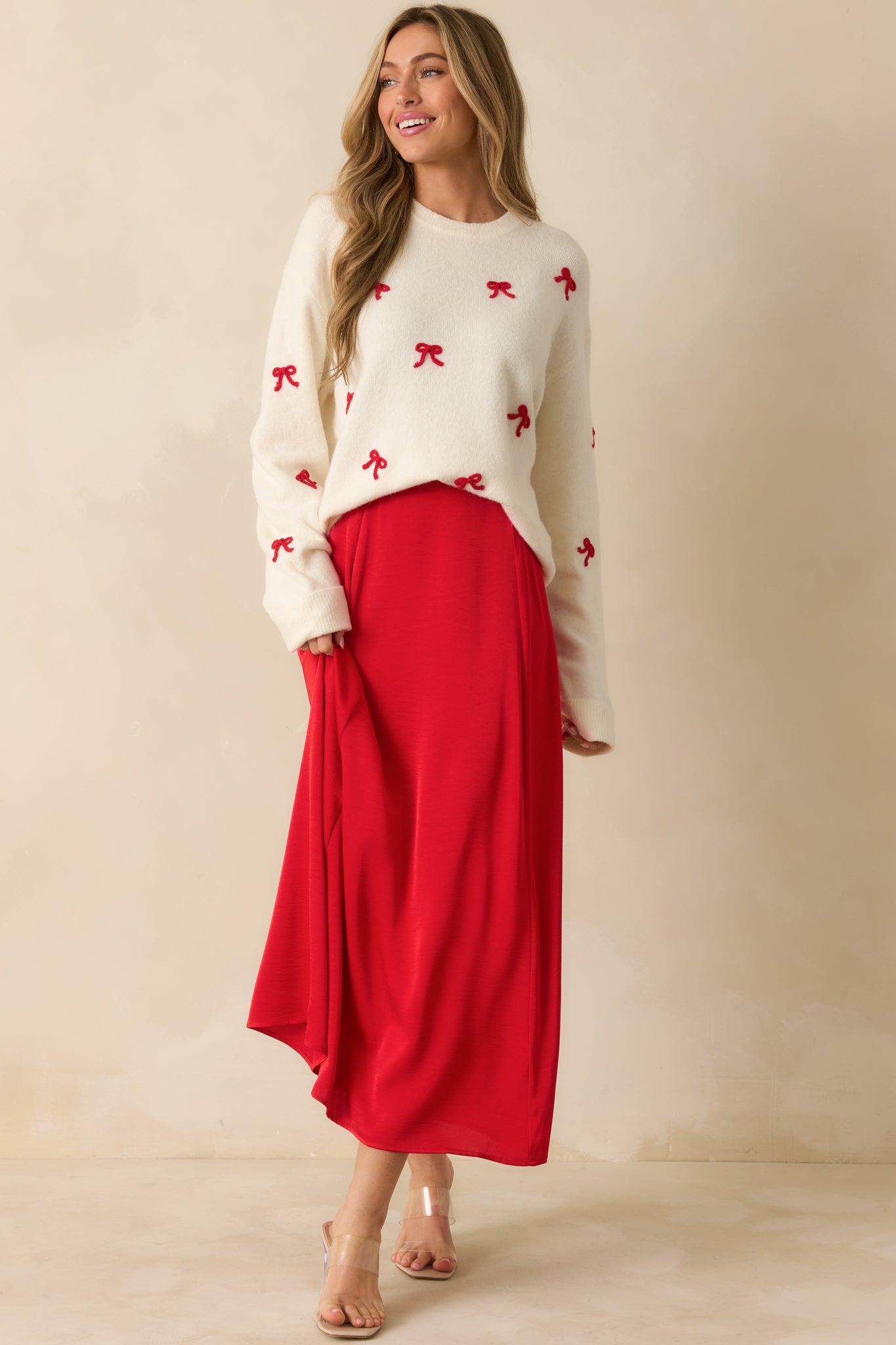 White festive sweater featuring crew neckline, long sleeves, and playful red bow embroidery on soft knit fabric.