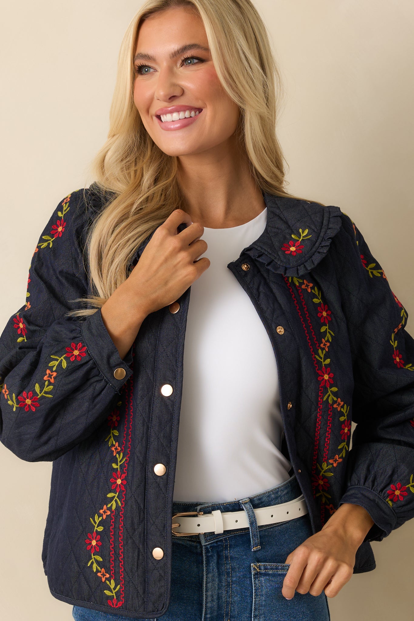 Cropped view of the quilted jacket showing buttoned cuffs, snap closure, and embroidered floral details.