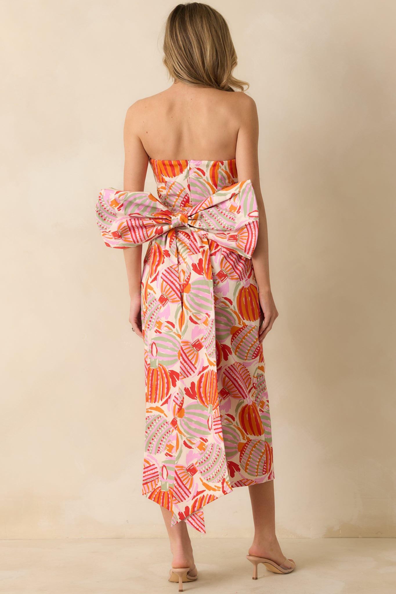 The back emphasizes the seam lines and zipper closure, with the oversized bow wrapping around the rear.