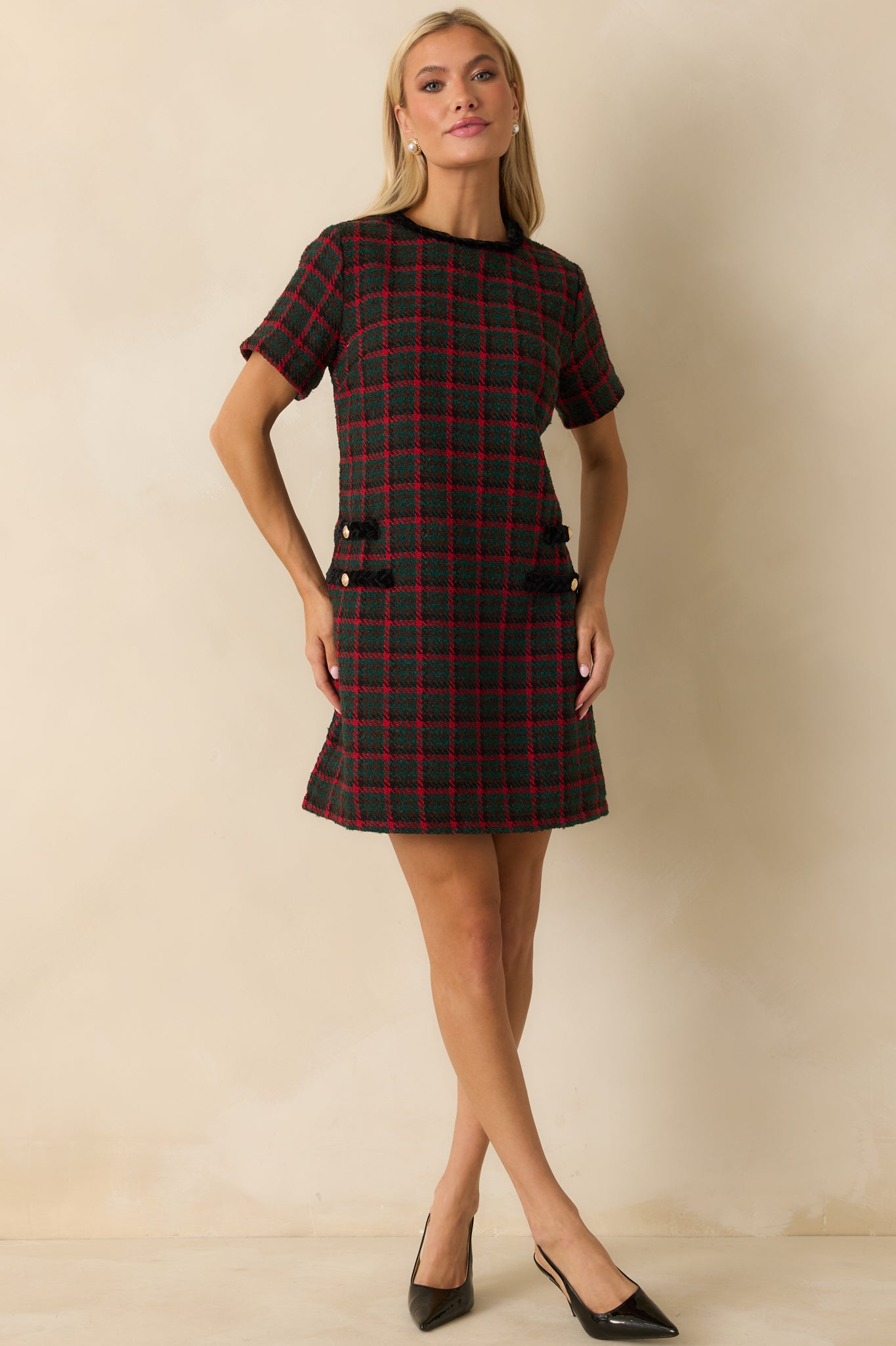 Tweed shift dress in green and red plaid highlighting its structured silhouette and the neatly trimmed pockets accented with gold buttons.