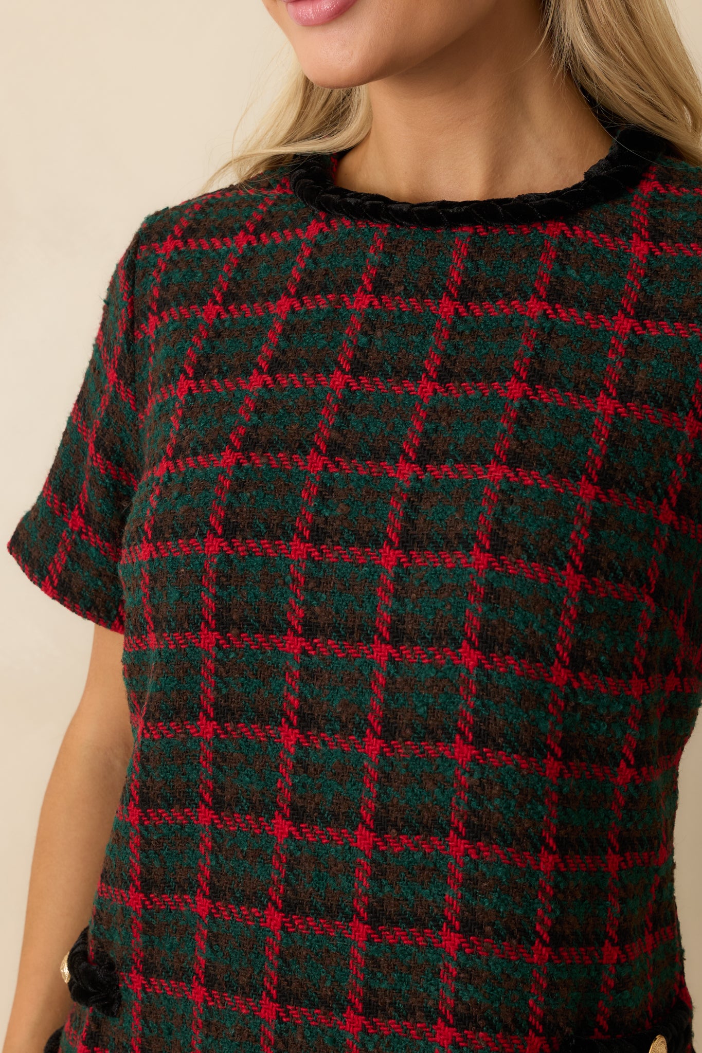 Close view of the tweed’s green and red plaid weave paired with the crisp contrast trim outlining the front pocket.