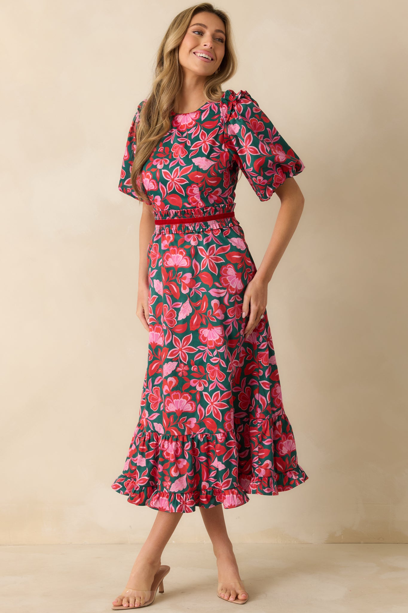 The dress highlights its puff sleeves, fitted elastic waist, and flowing tiered ruffle hem with green and pink floral print.