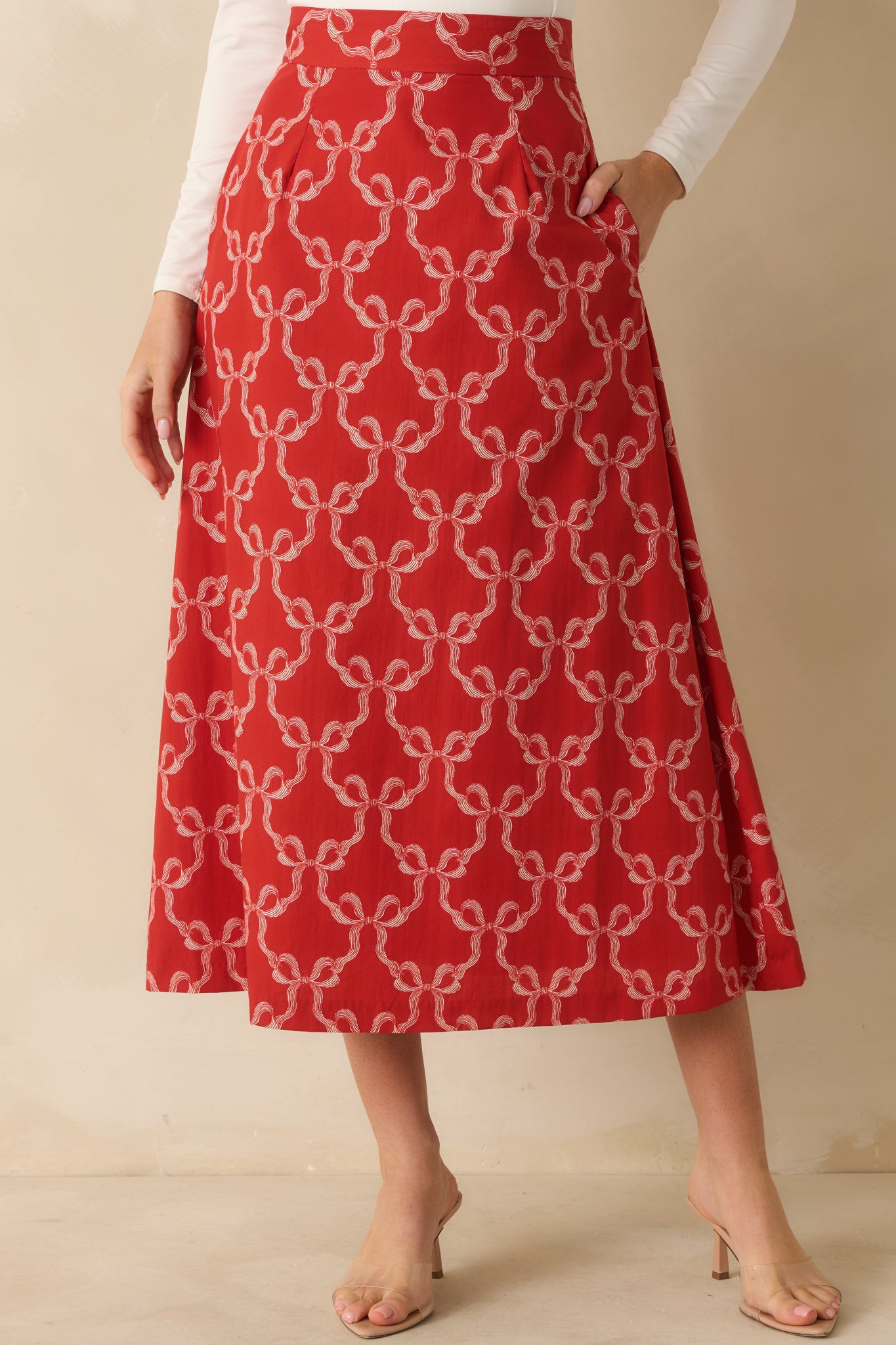 The red midi skirt shows its allover bow print with a structured A-line silhouette and fitted waistband.