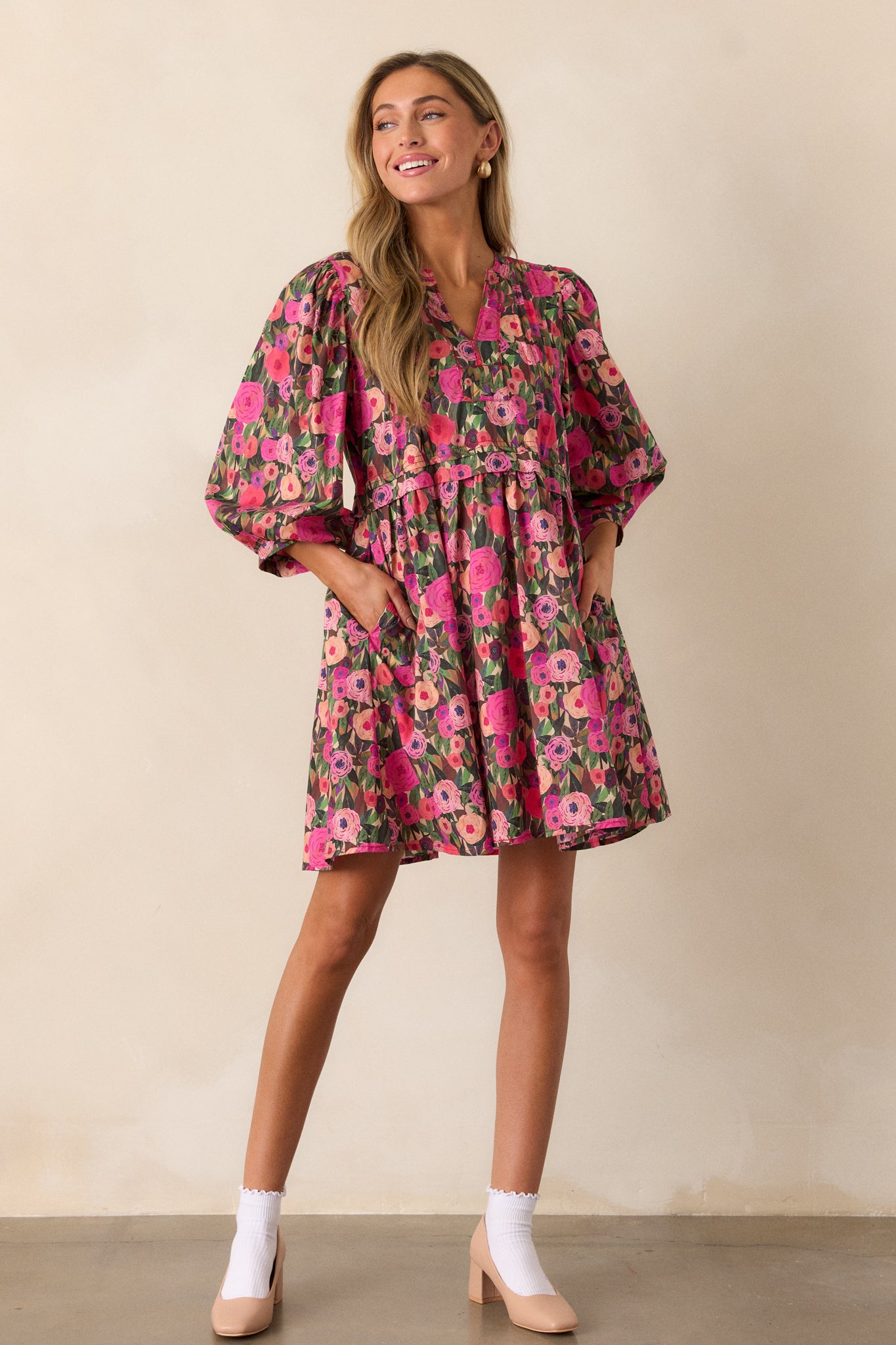 A full view of a pink mini dress with a split neckline, featuring a vibrant floral print and 3/4 puff sleeves.