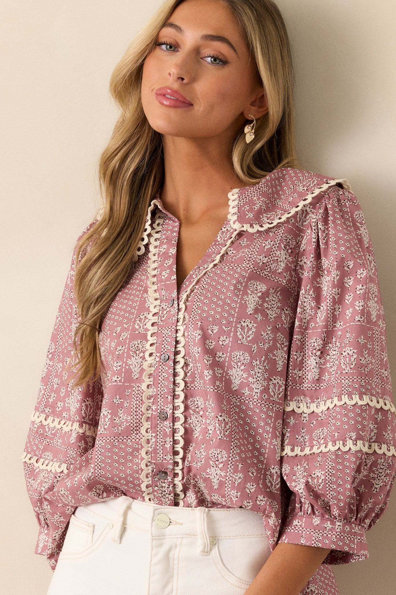 This dusty pink blouse features a collared v-neckline, button up front, small scalloped hemming, a beautiful floral pattern, and 3/4 puff sleeves with scalloped detailing.