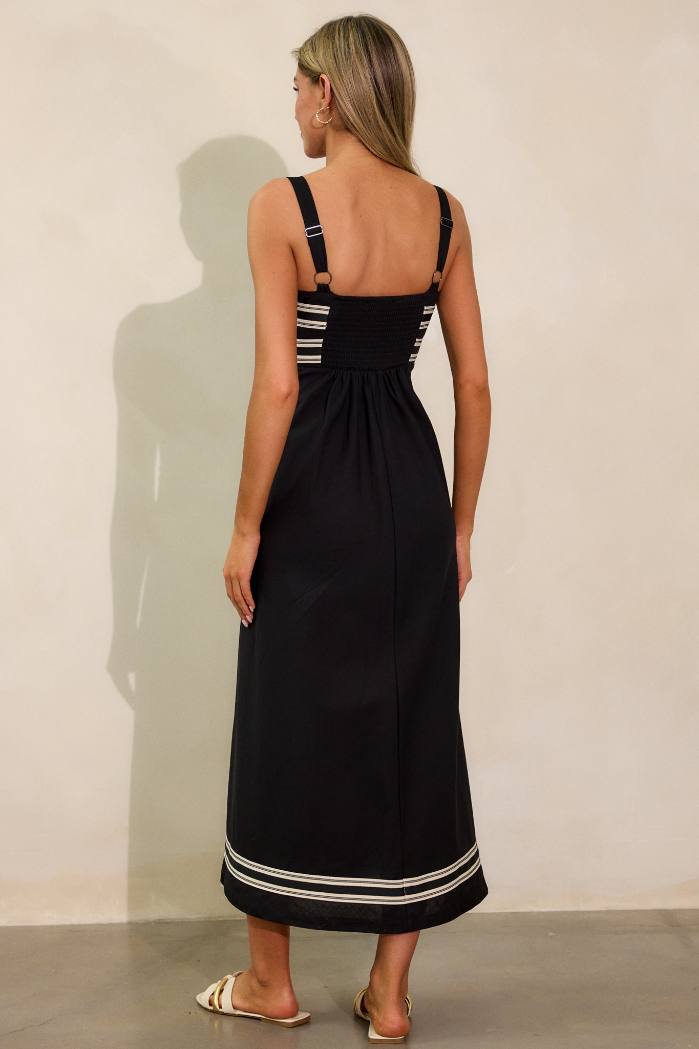 Complete back view of the black dress, emphasizing the smocked back panel and adjustable wide straps for a customized fit.