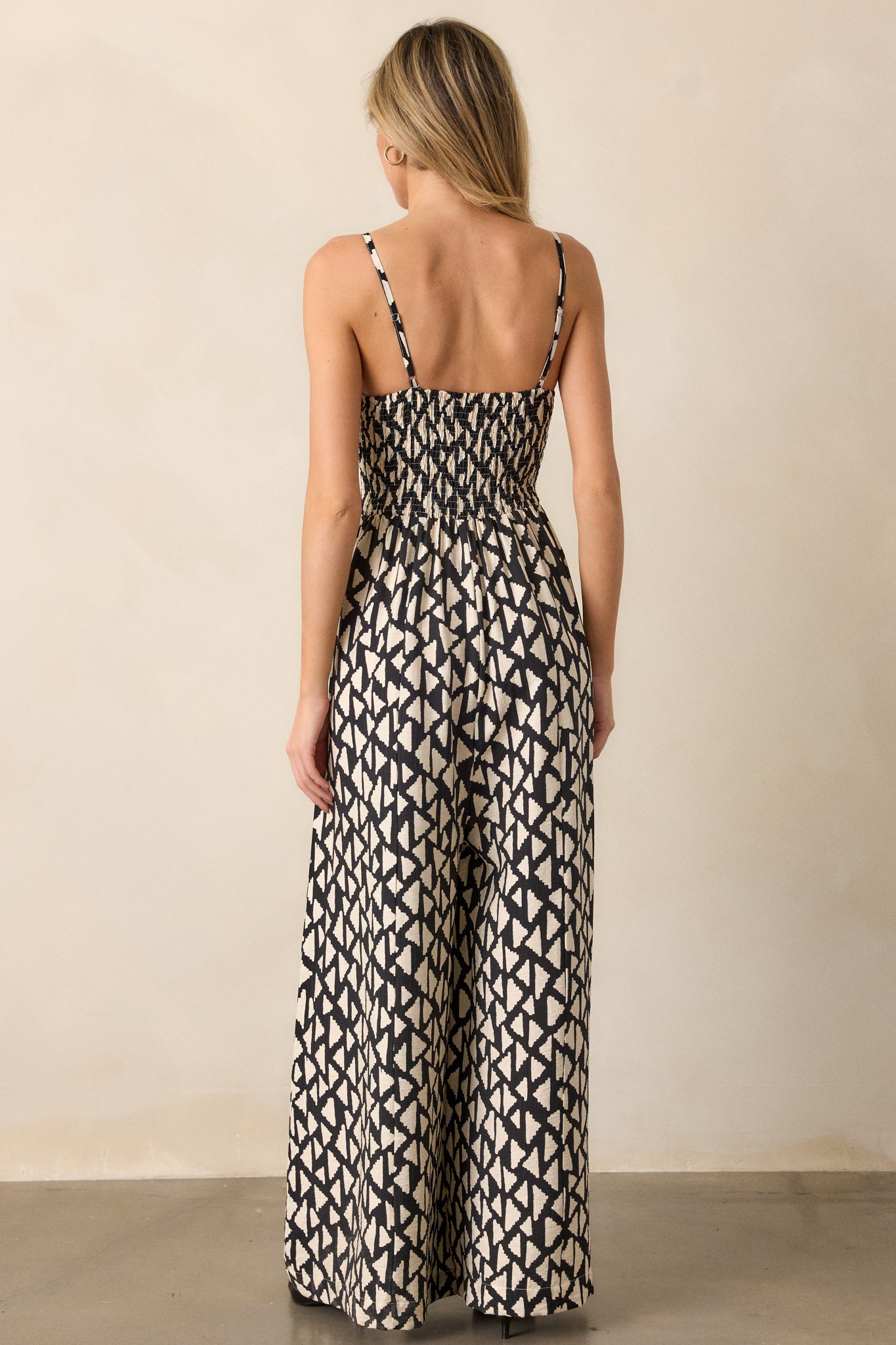 Another back view of the black jumpsuit highlighting the allover geometric pattern, adjustable straps, and flowing wide-leg pants.