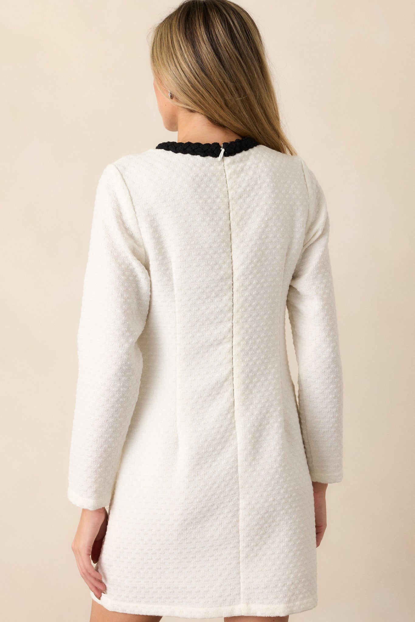 Back view of the ivory tweed mini dress, displaying the discrete back zipper and the continuity of the black trim along the neckline and sleeves from behind.