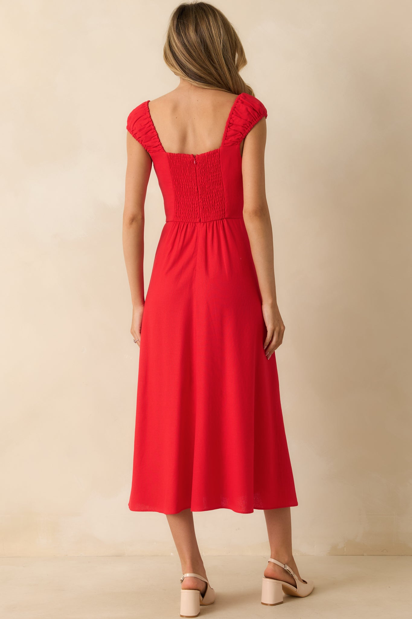 Rear view of the red midi dress highlighting the smocked back, hidden zipper, and flowing skirt with slit.